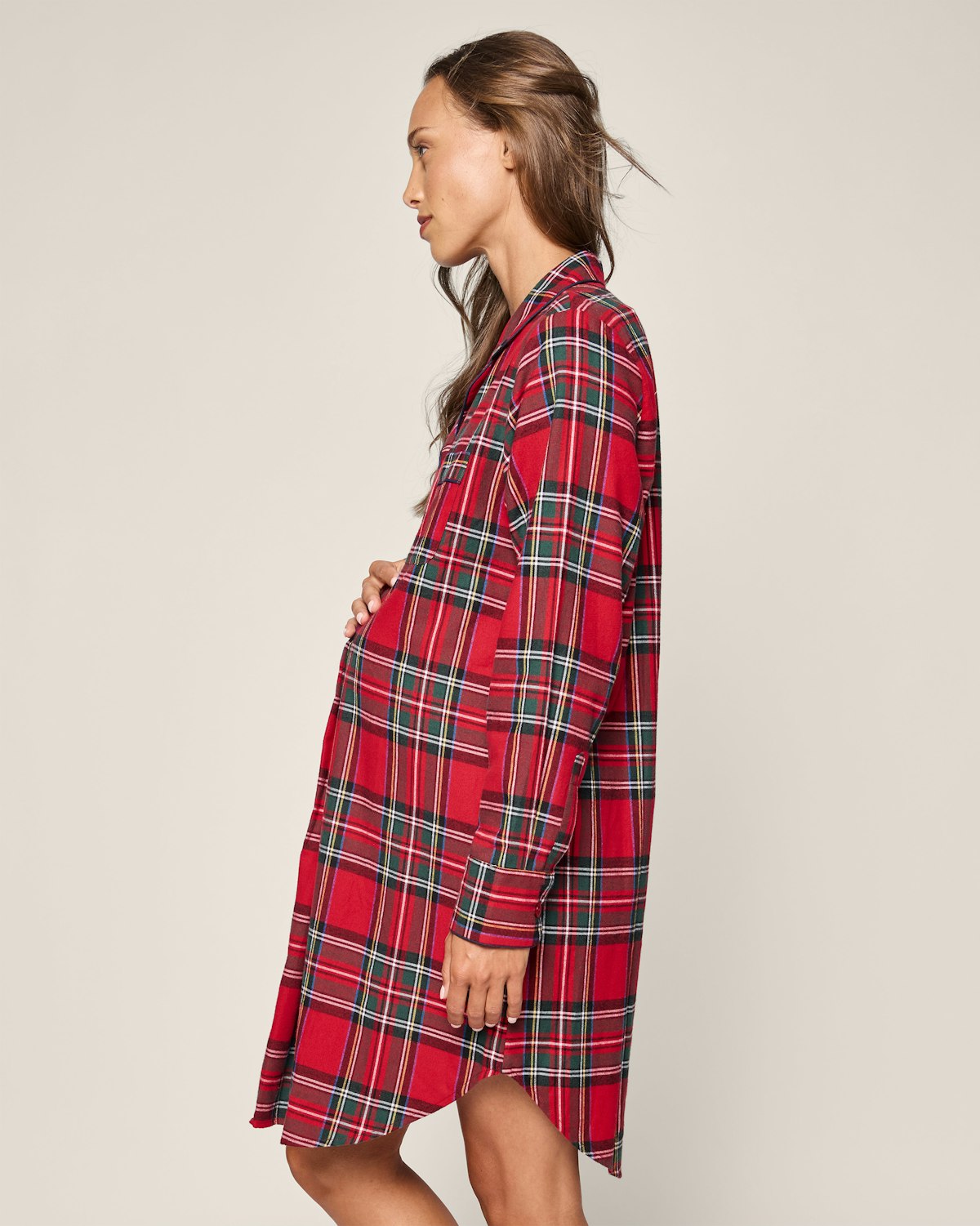 A person in profile gently touches their belly, wearing a Petite Plume Womens Brushed Cotton Maternity Nightshirt in Imperial Tartan against a plain neutral background.