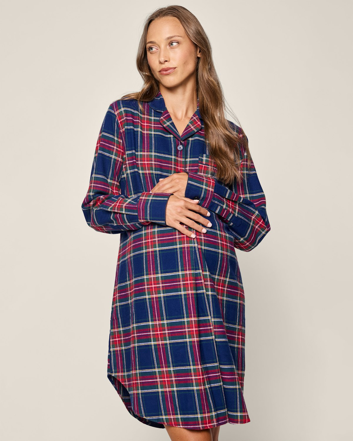 A woman models the Womens Brushed Cotton Maternity Nightshirt in Windsor Tartan by Petite Plume. She stands against a neutral background, with loose long hair, elegantly holding the nightshirt and looking to the side, evoking luxury akin to high-quality cotton sleepwear.
