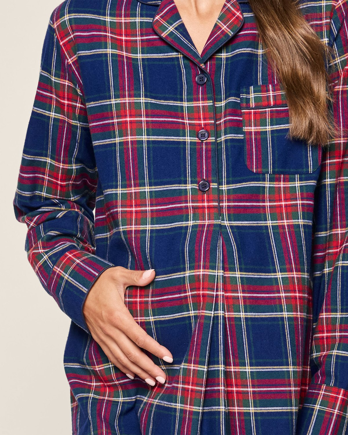 A person wears the Womens Brushed Cotton Maternity Nightshirt in Windsor Tartan by Petite Plume, featuring blue and red plaid, a breast pocket, long sleeves, and a collar. Their right hand holds the side of this luxurious cotton garment.
