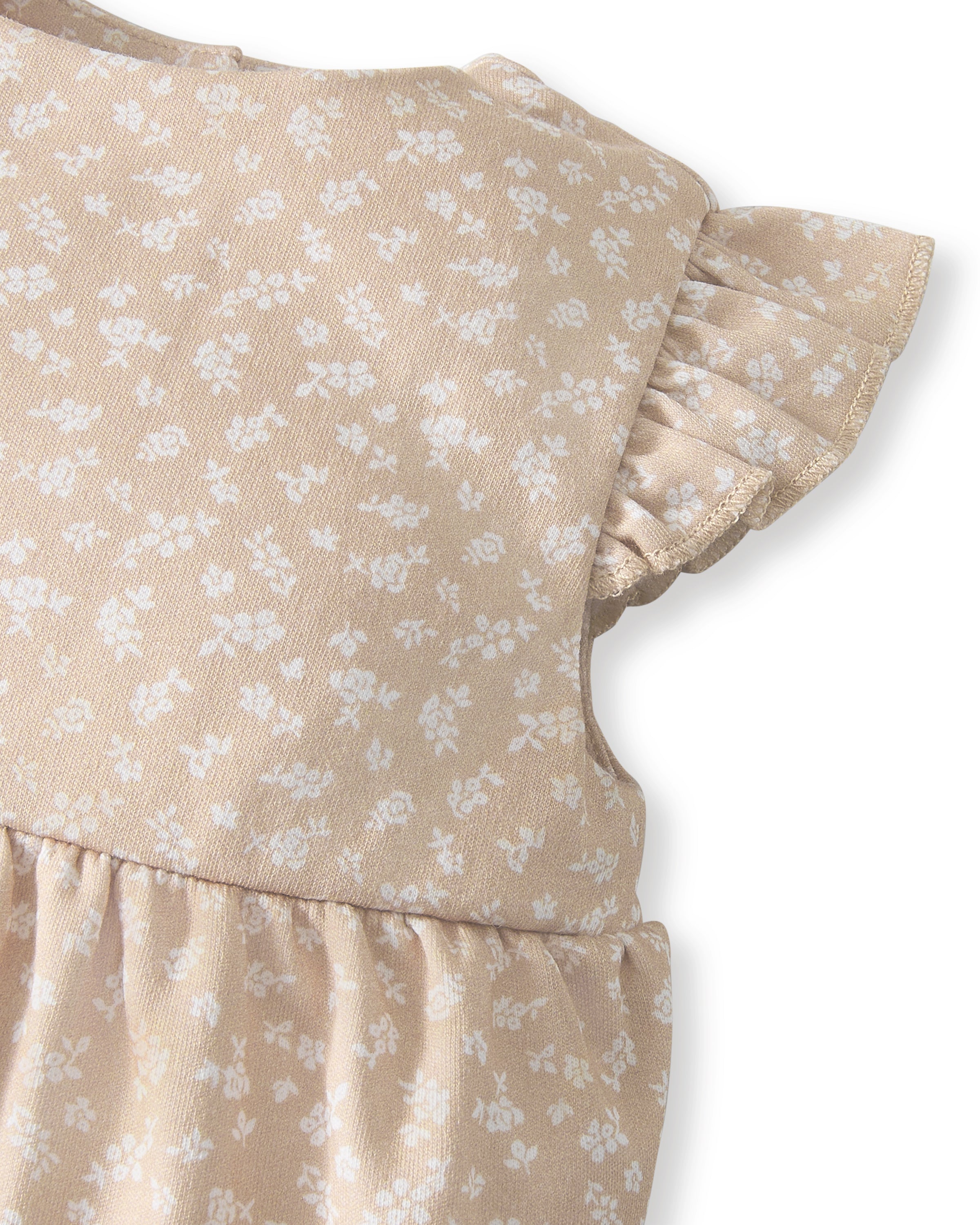 The Baby's Pima Isla Play Romper in Ditsy Waltz Camel features a beige base with white florals, short ruffled sleeves, gathered waist, and elastic leg openings. Made from soft, lightweight fabric—ideal for warm weather—it's shown laid flat on a white background.