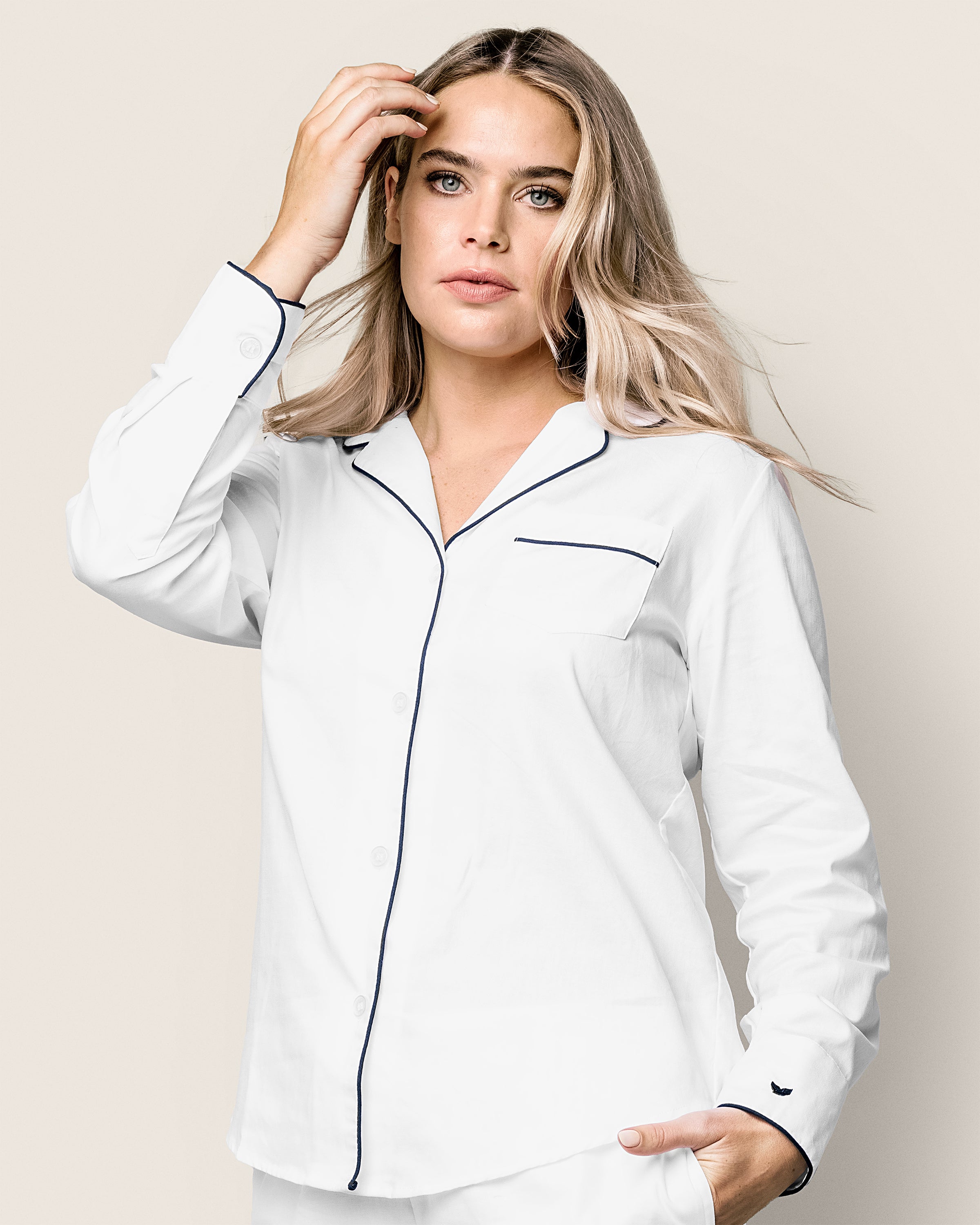 A woman with long blonde hair models the Petite Plume Womens Pima Long Sleeve Short Set in White with Black Piping. She stands gracefully, one hand in her hair and the other in a pocket, against a plain, light background.