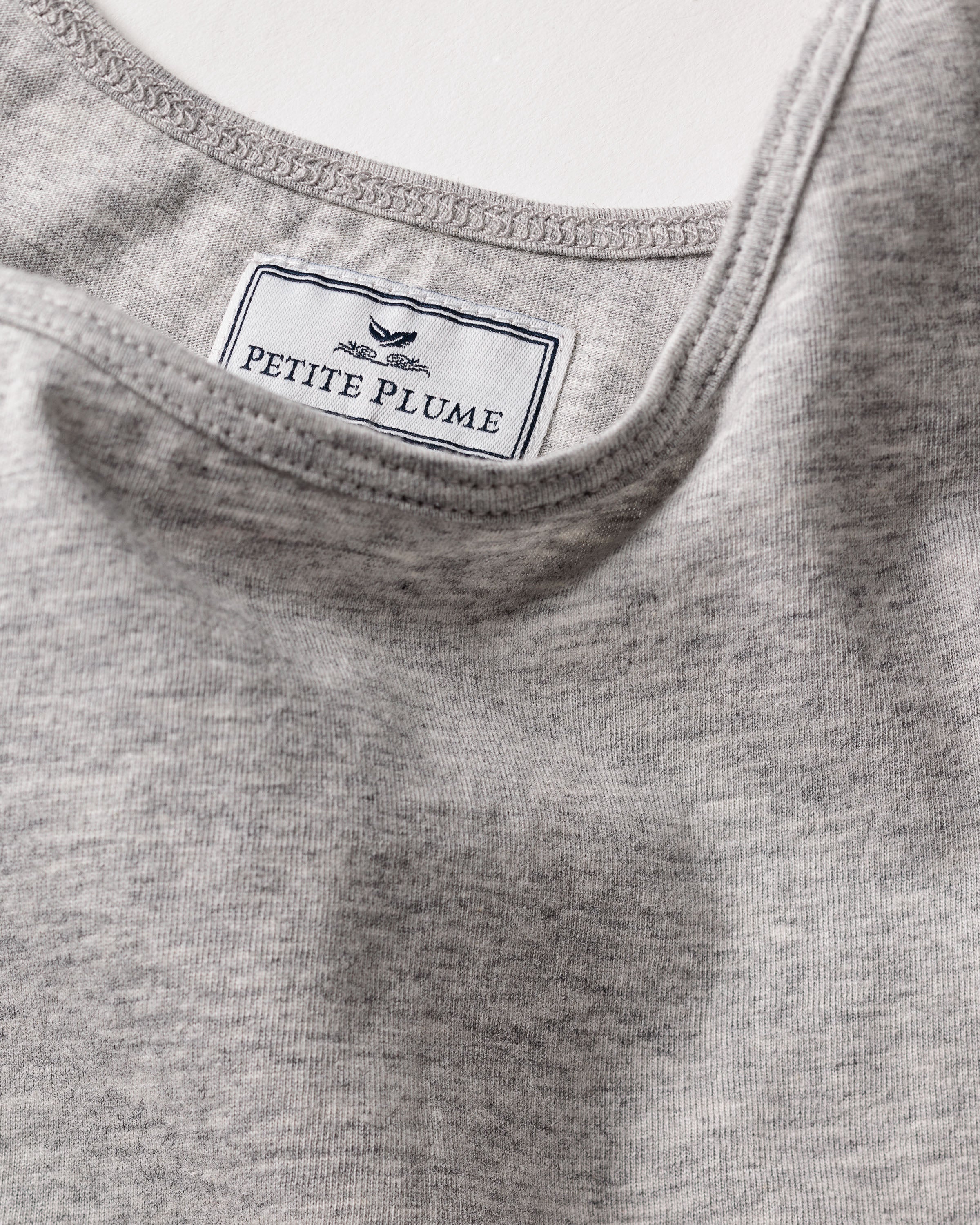 Close-up of the Womens Pima Tank Top in Light Grey from Petite Plume, featuring a label inside with a design and Petite Plume text. Made of lush Peruvian Pima cotton, the fabric looks soft and elegantly spread on a flat surface.