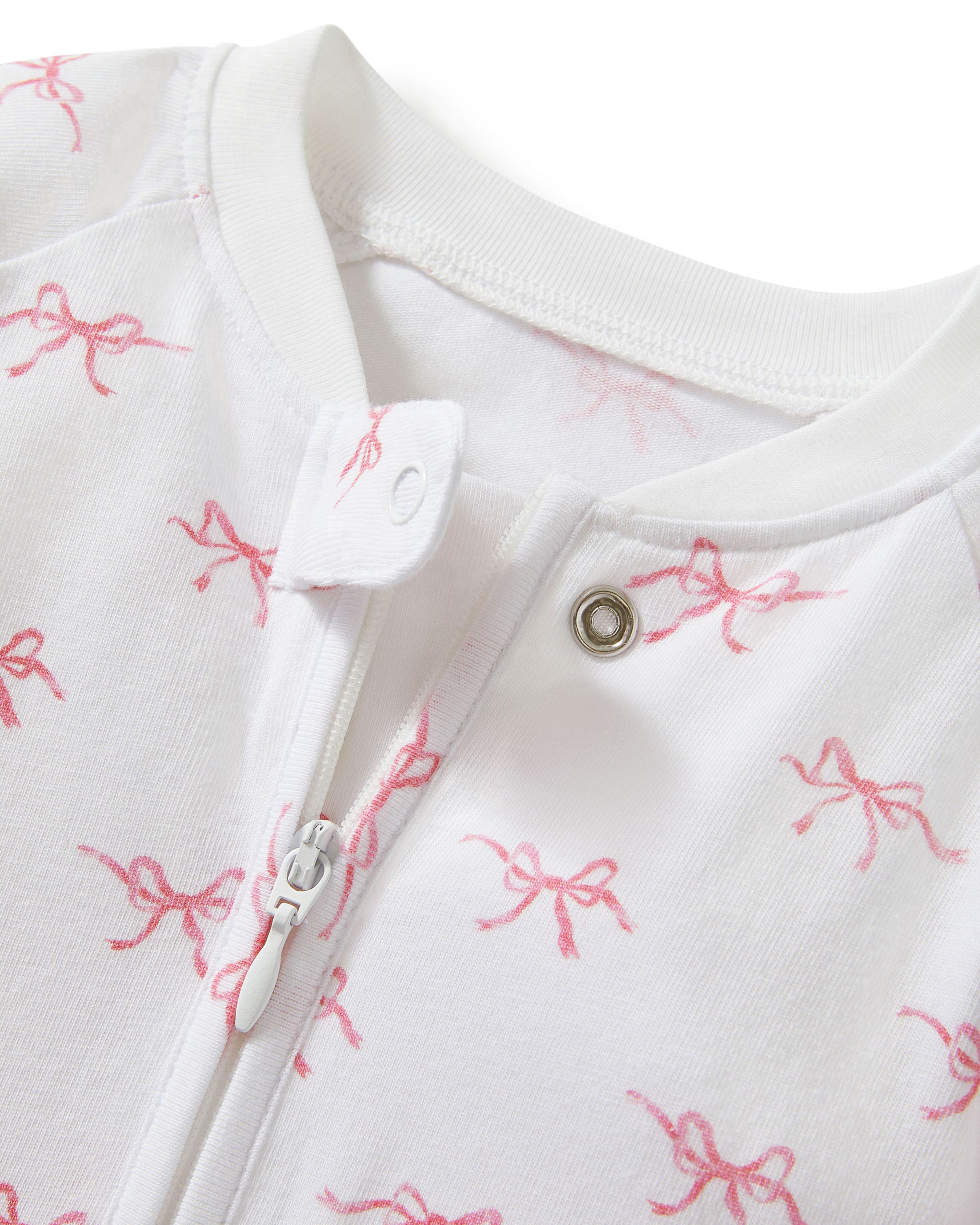 The Baby's Pima Peekaboo Romper in Blushing Bows is a white onesie with long sleeves and legs, accented by white cuffs and an angled zipper, and features a pink bow pattern.