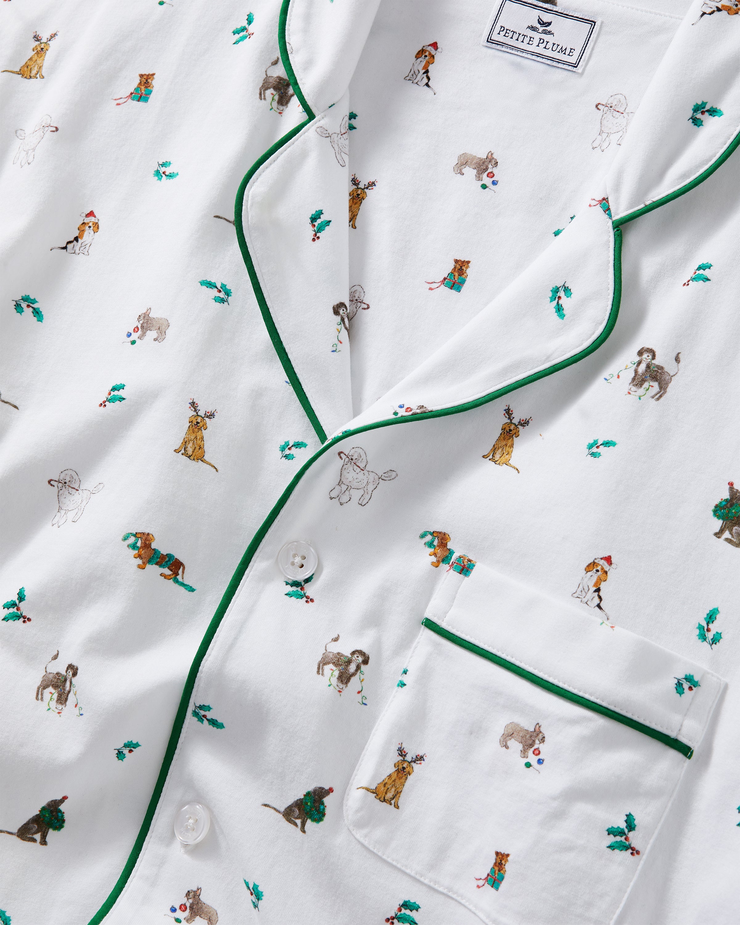 A person smiles in Petite Plumes Mens Pima Pajama Set in Jingle Paws, featuring colorful animal designs on soft Peruvian Pima cotton with green piping and a chest pocket against a plain, light background, enhancing their cheerful appearance.