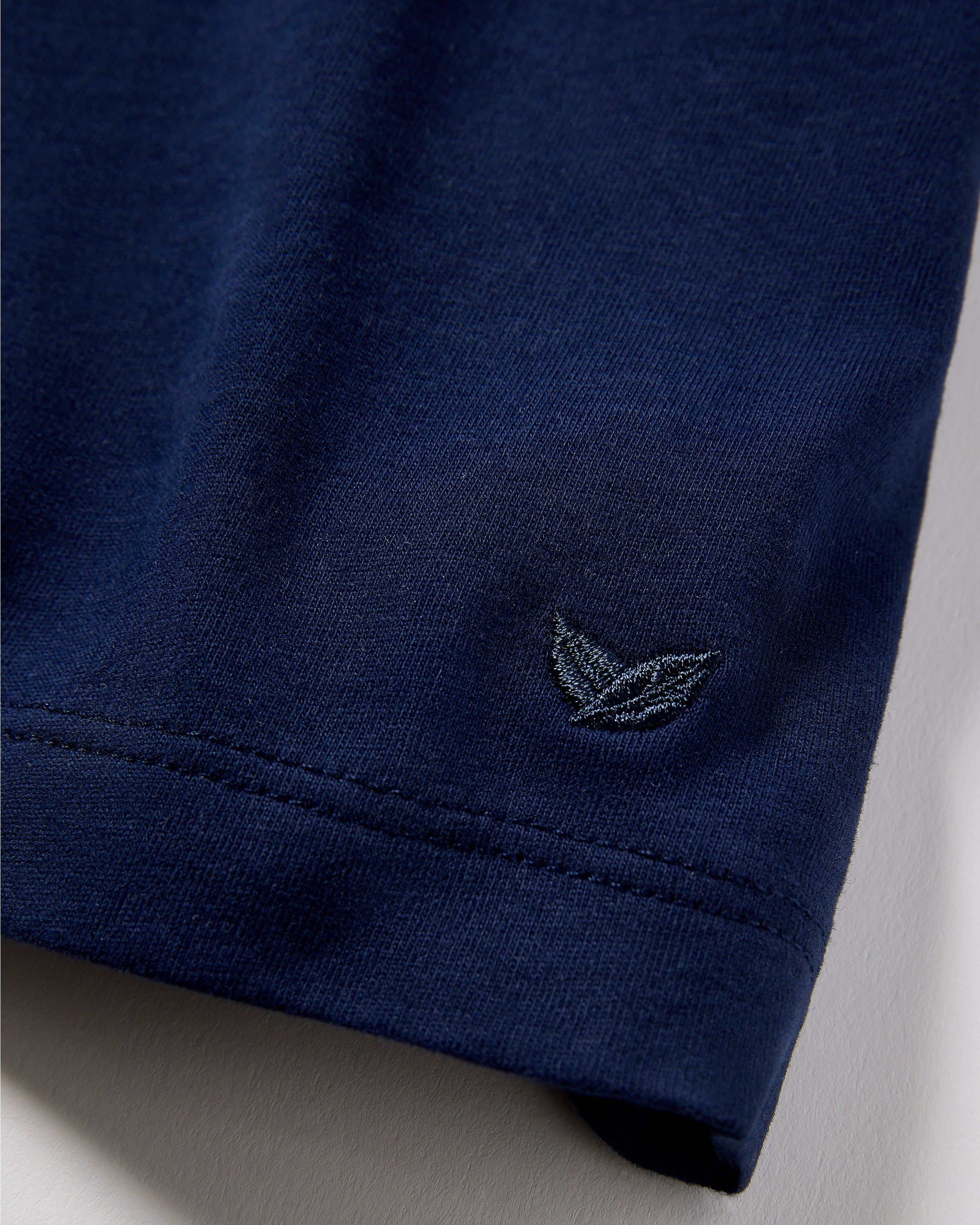 A close-up of the hem of the Mens Pima Crew Neck Short Sleeve Top in Navy by Petite Plume, showing a subtle embroidered design of overlapping leaves in slightly lighter blue thread on yarn-dyed Peruvian Pima cotton fabric.
