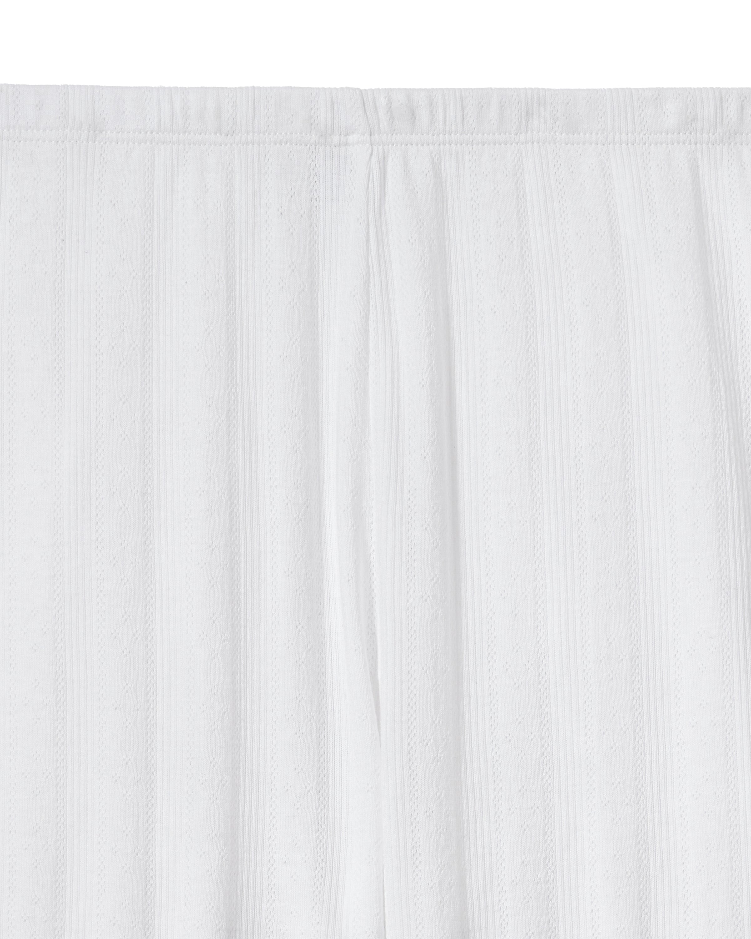 A woman stands barefoot on a light background wearing the Women's Pointelle Pant in White, paired with a sleeveless white tank top, posing with a relaxed and neutral expression.