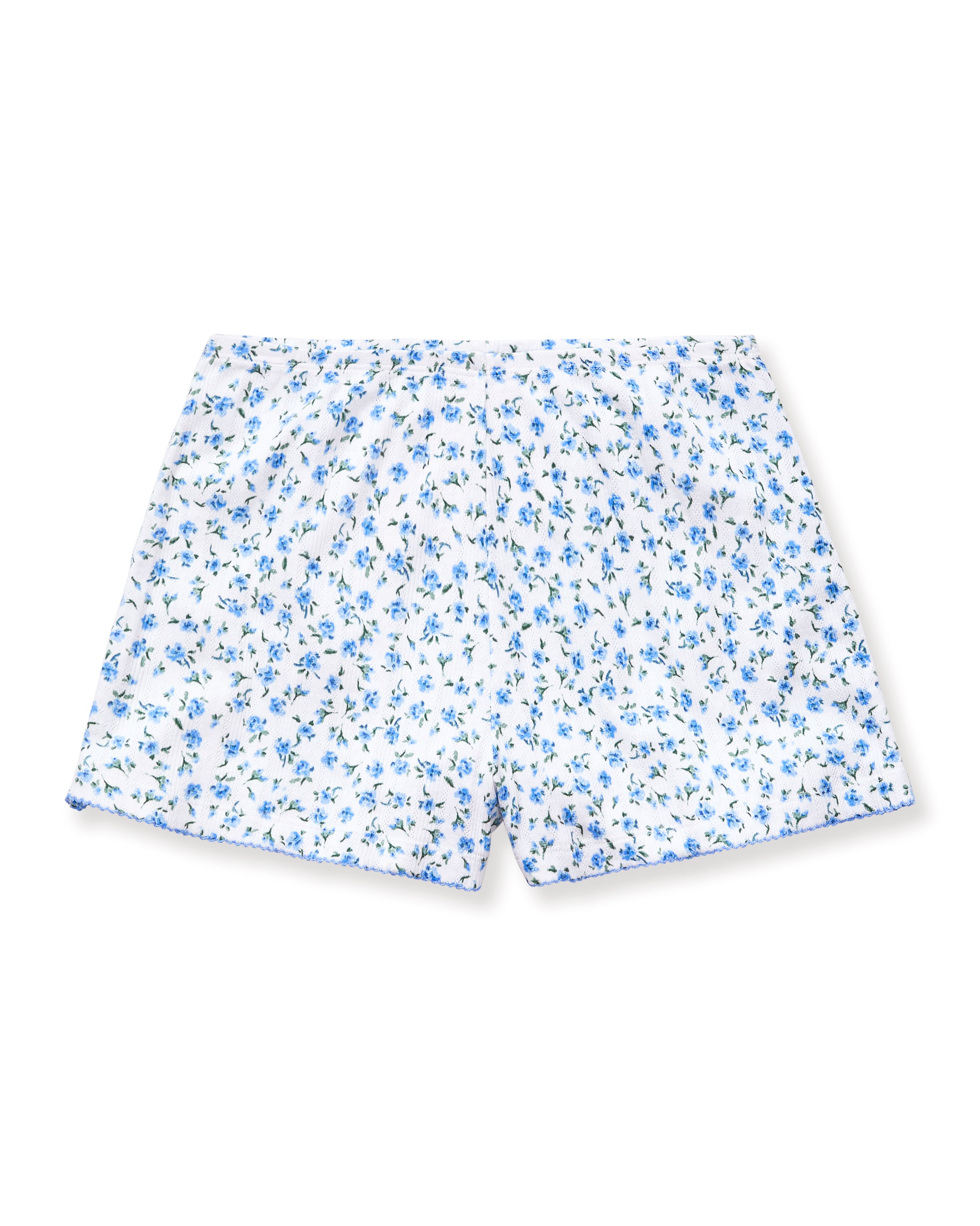 A person stands barefoot against a plain background, wearing Women's Pointelle Shorts in Blue Floral with a matching short-sleeve top. They have long, wavy hair and a relaxed, neutral expression.