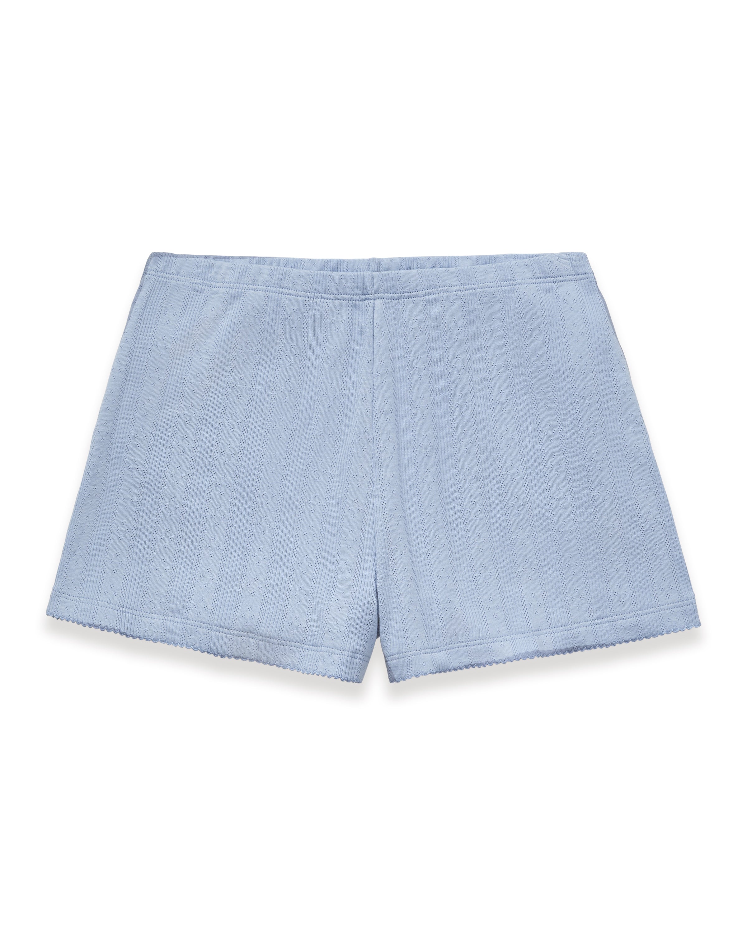 A woman with long wavy hair stands barefoot on a plain background, wearing Women's Pointelle Shorts in Periwinkle and a matching light blue ribbed tank top. She has a relaxed, neutral expression.