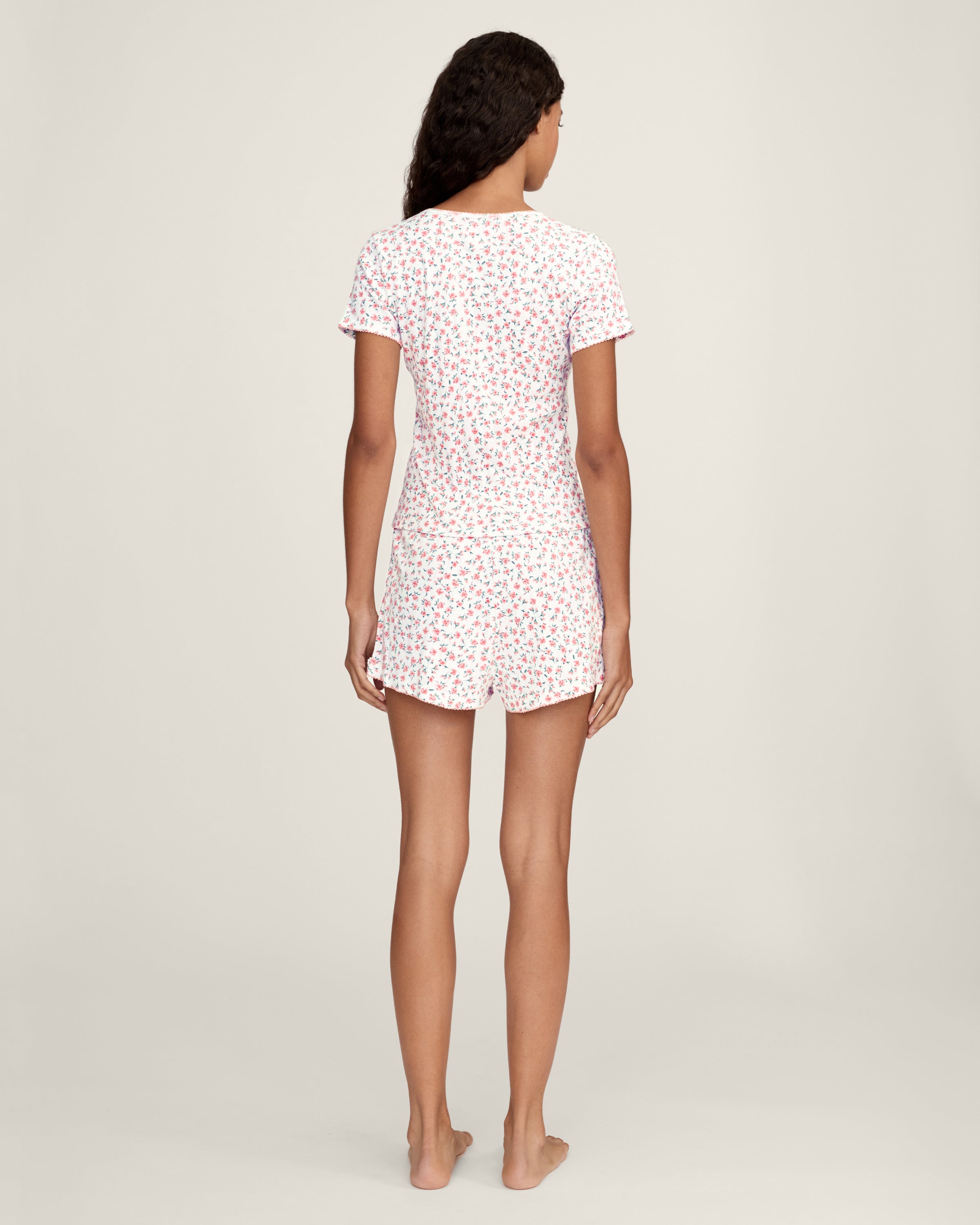 A woman with long curly hair wears the Women's Pointelle T-Shirt in Pink Floral, standing against a plain light background.