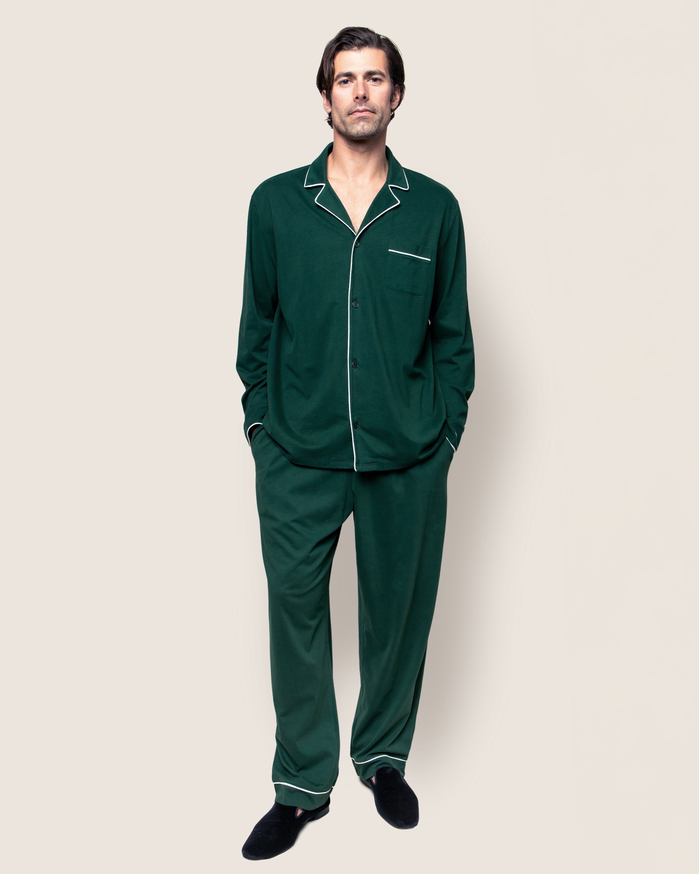The Mens Pima Pajama Set in Evergreen by Petite Plume is crafted from luxury Peruvian Pima cotton. This timeless set includes a dark green long-sleeve button-up top with white piping and a chest pocket, paired with matching pants featuring an elastic waistband, on a pristine white background.