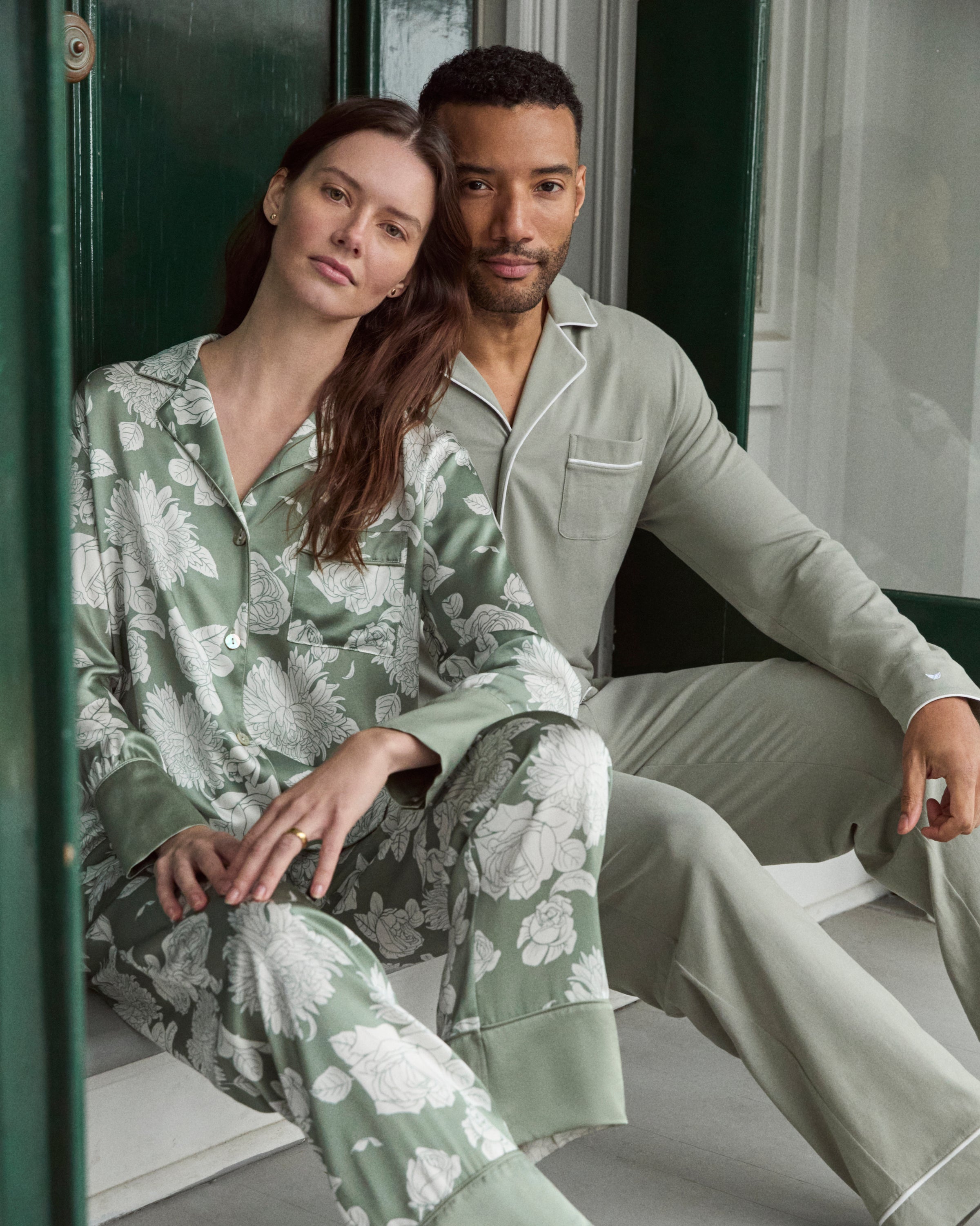 Women's Silk Pajama Set in Sage Bloom: a sage green satin set with a white floral pattern, featuring a long-sleeve button-up top with chest pocket and matching drawstring pants.