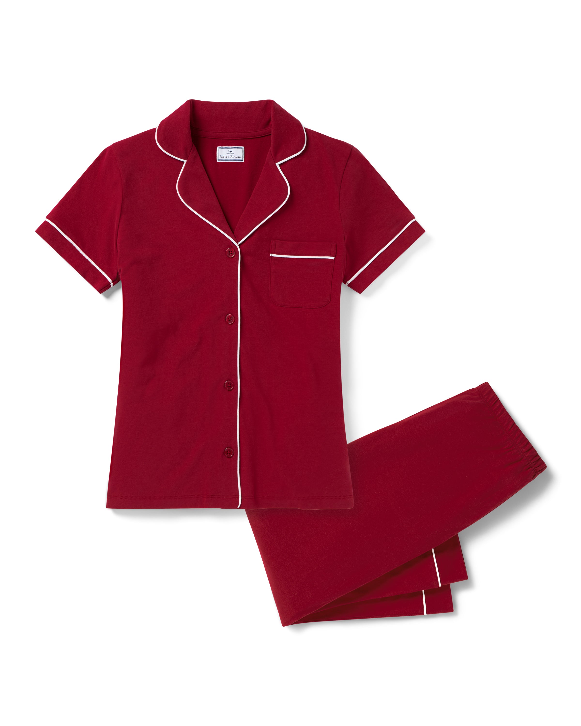 The Women's Pima Crop Pajama Set in Bordeaux features red short-sleeve, white-piped button-up top with a chest pocket and matching long pants, all laid flat on a white background.