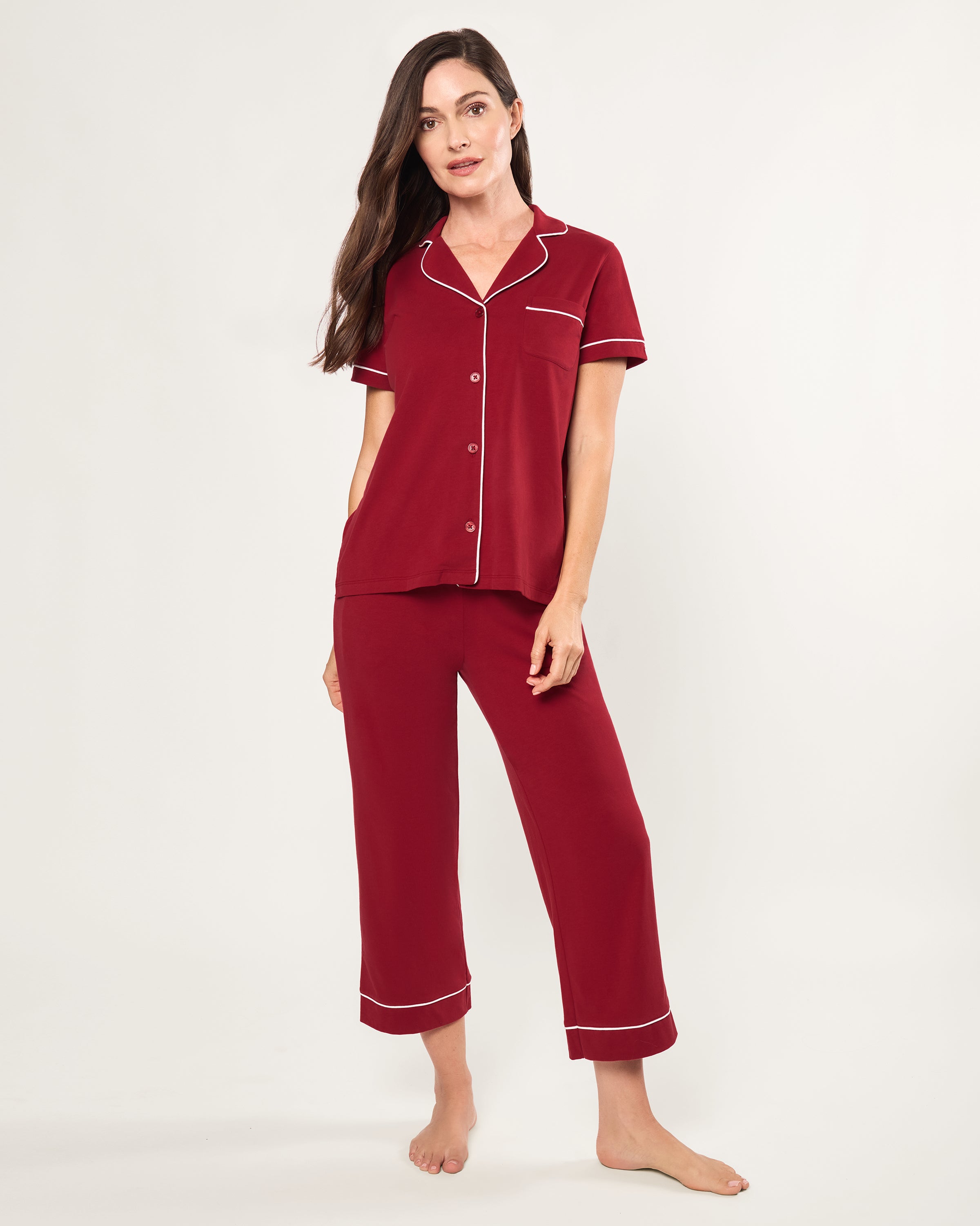 The Women's Pima Crop Pajama Set in Bordeaux features red short-sleeve, white-piped button-up top with a chest pocket and matching long pants, all laid flat on a white background.
