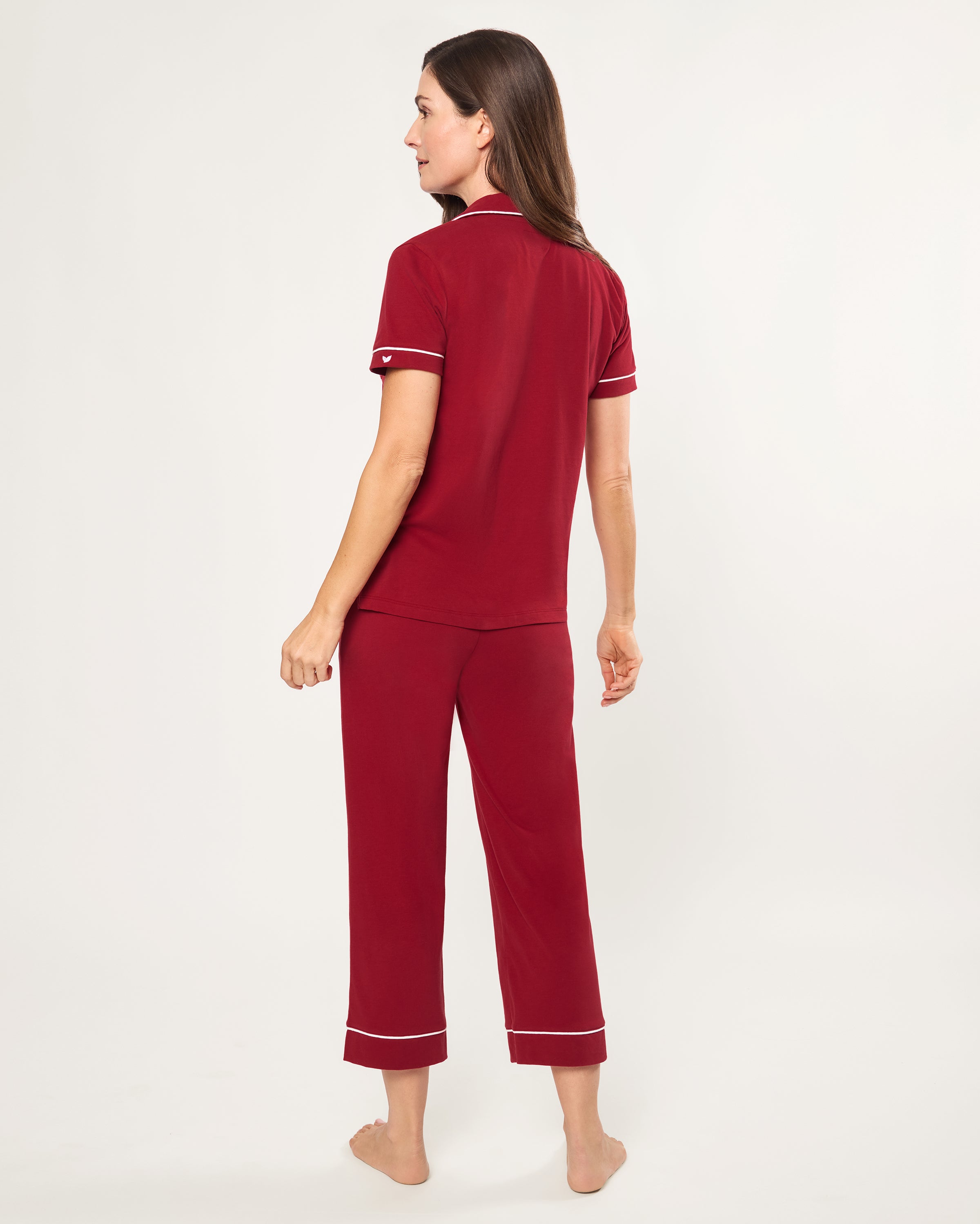 The Women's Pima Crop Pajama Set in Bordeaux features red short-sleeve, white-piped button-up top with a chest pocket and matching long pants, all laid flat on a white background.