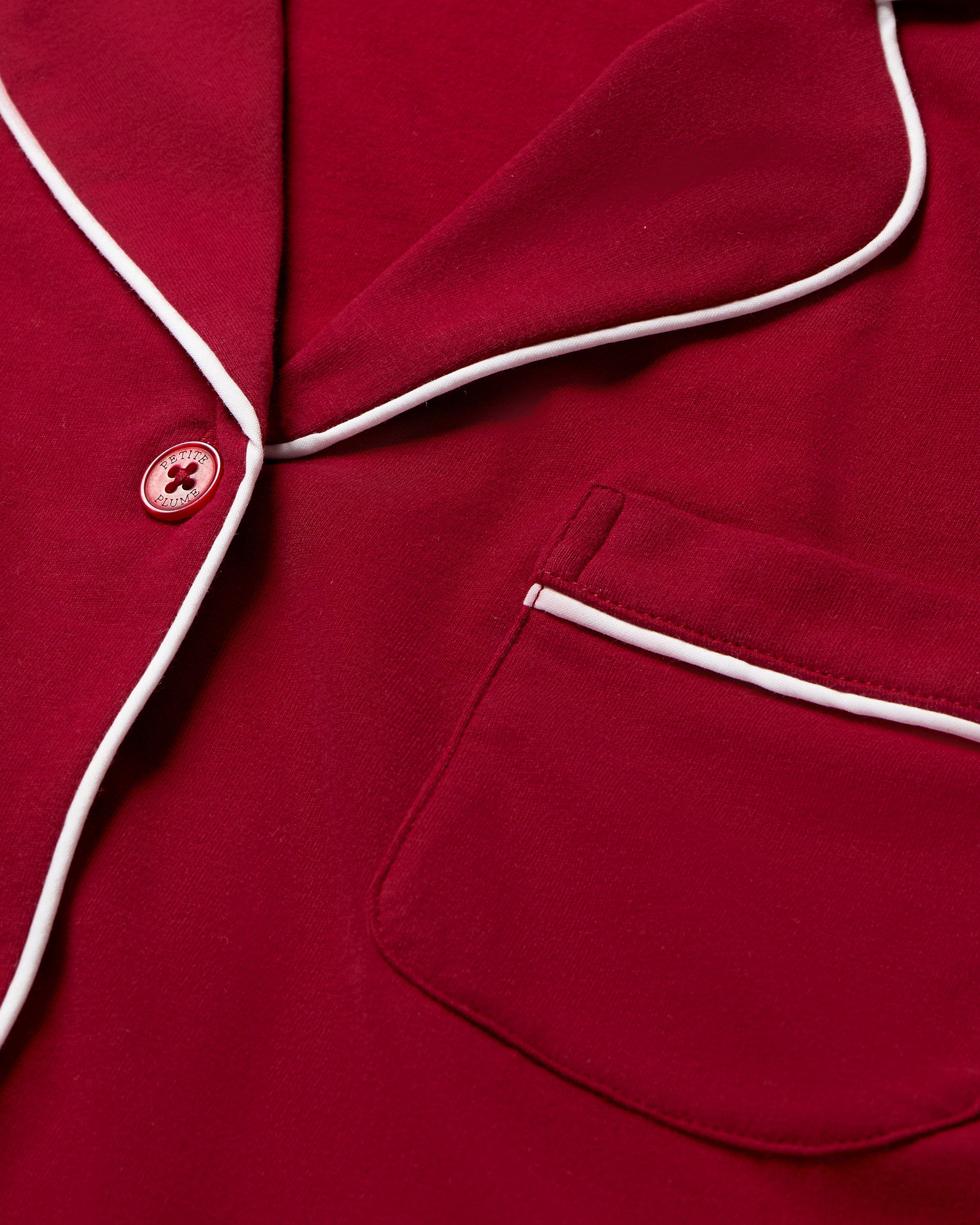 The Women's Pima Crop Pajama Set in Bordeaux features red short-sleeve, white-piped button-up top with a chest pocket and matching long pants, all laid flat on a white background.