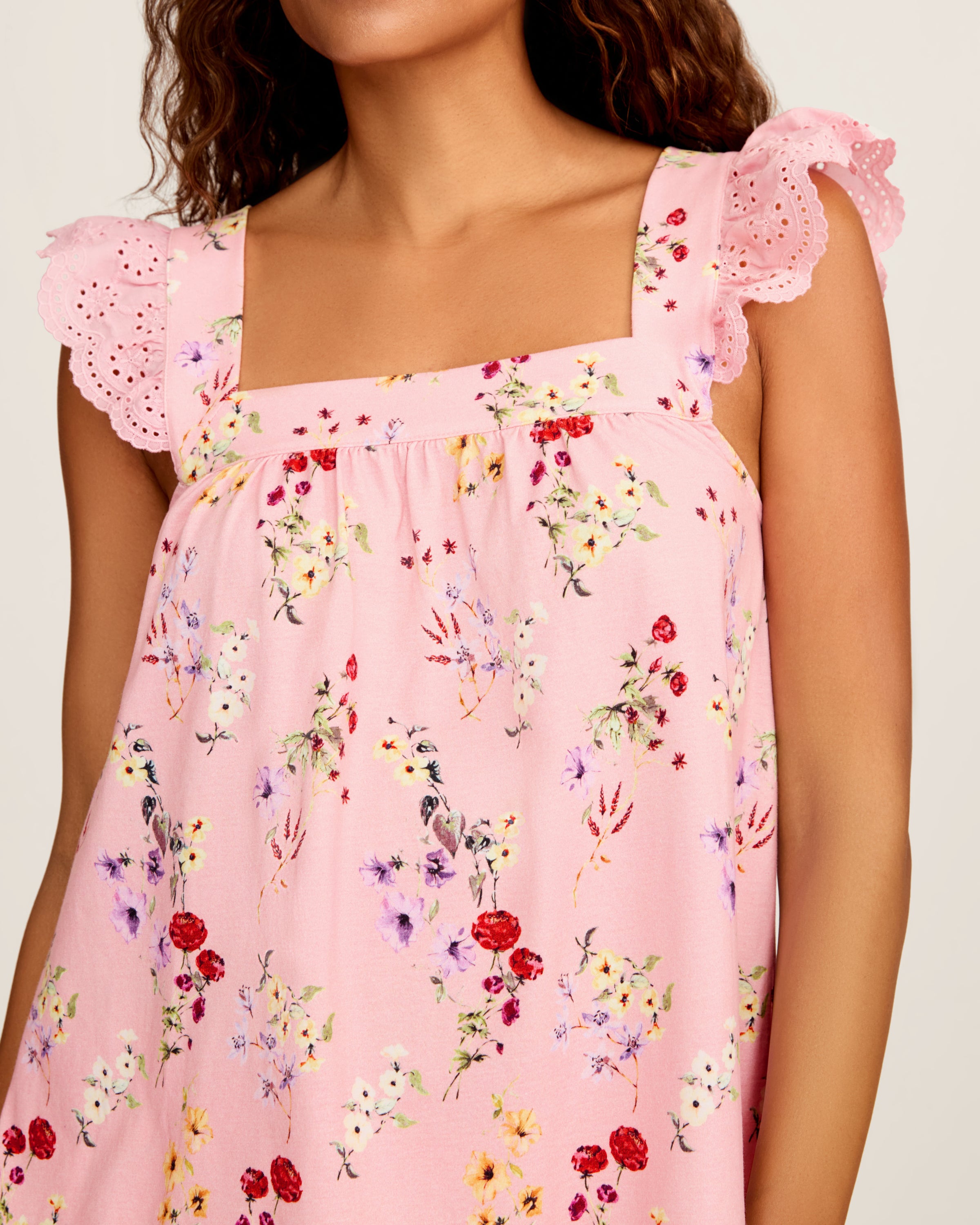 The Women's Pima Clara Short Set in Brilliant Botanical Blush features a matching pink pajama set with a sleeveless top, ruffled straps, and shorts, both adorned with a colorful botanical print.