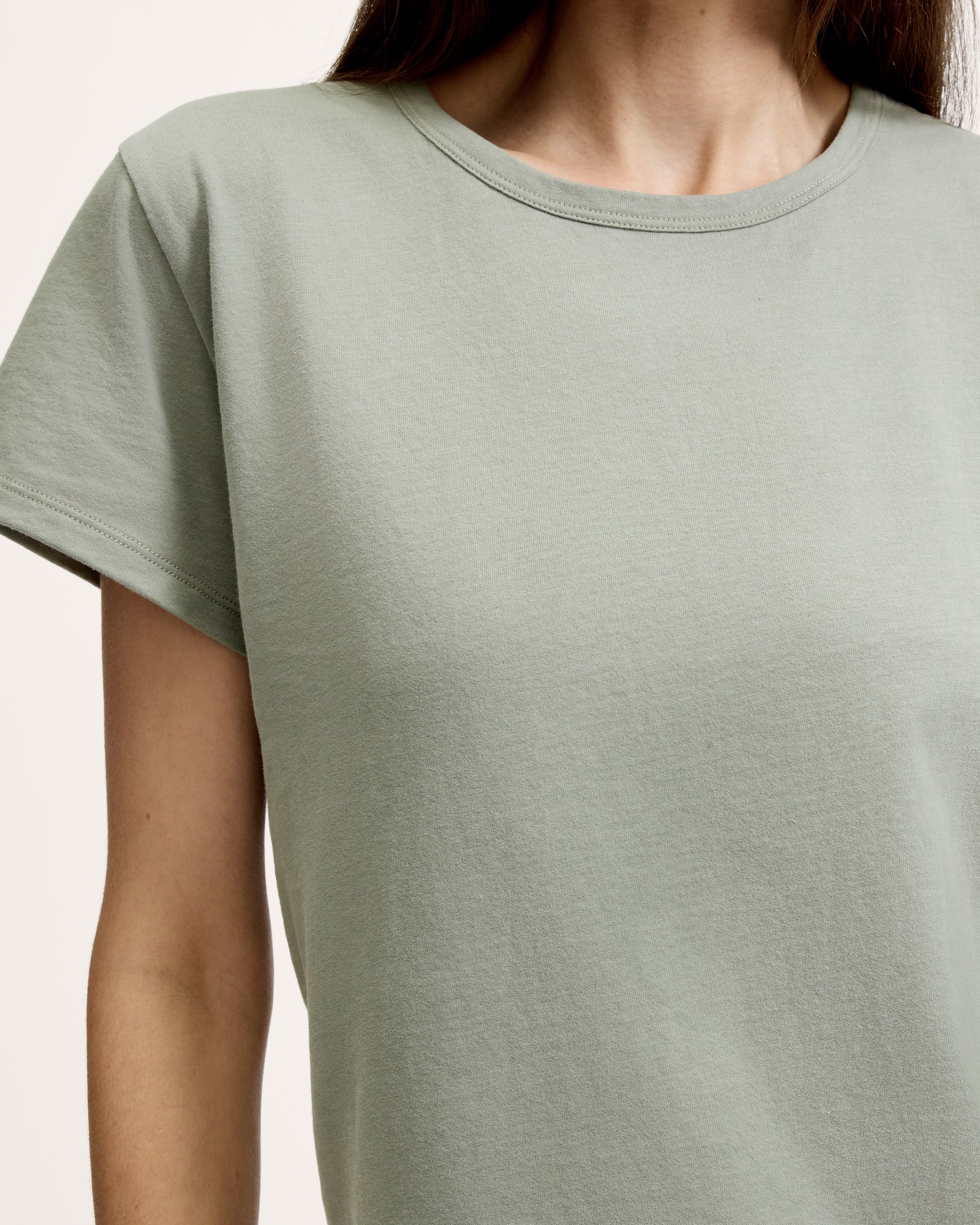 A woman with straight brown hair wears the Women's Pima Essential Crew Neck Tee in Sage and matching drawstring shorts, standing with her hands on her hips against a plain light background.