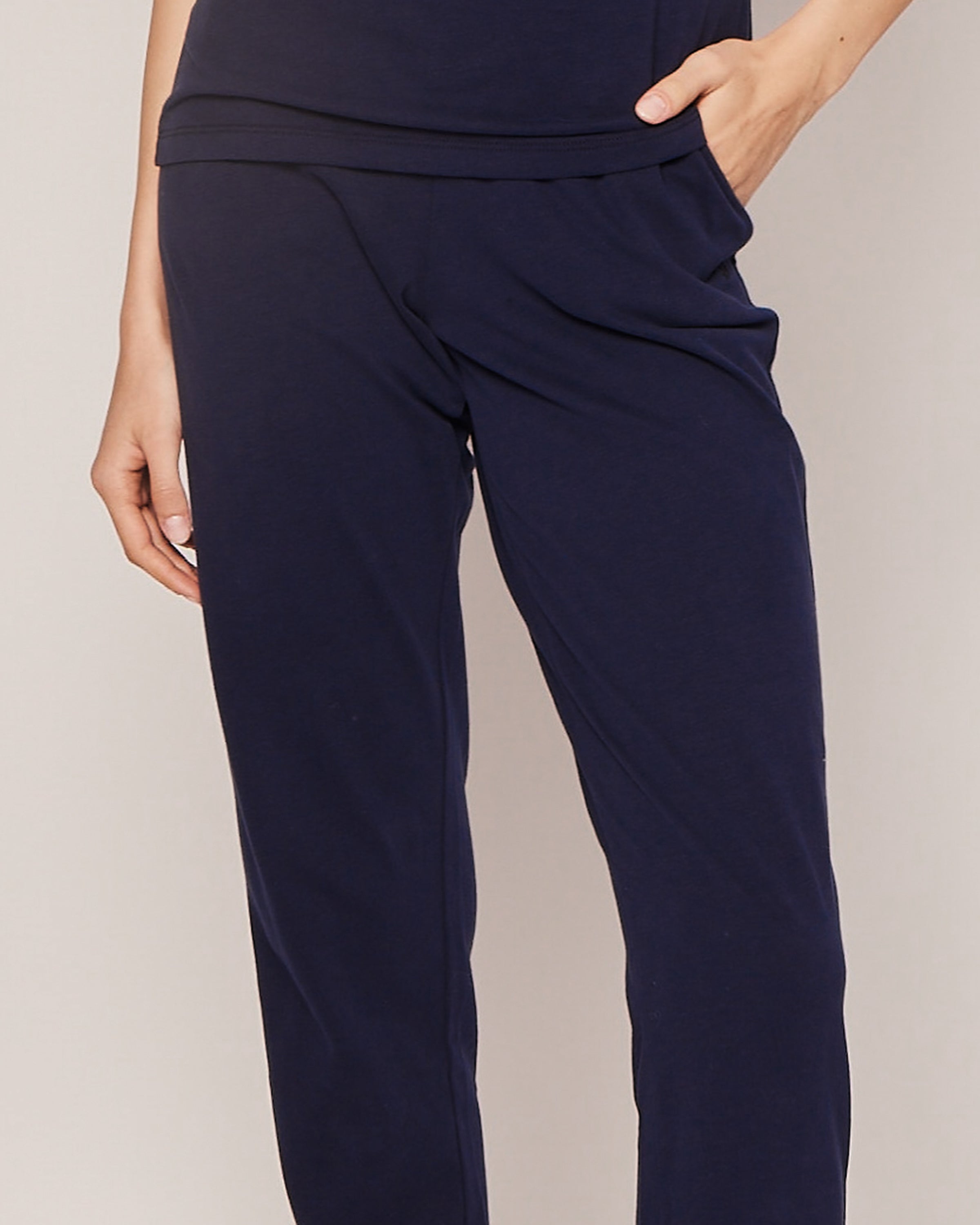 A person models Petite Plumes Womens Pima Lounge Pants in luxurious navy Peruvian Pima cotton against a neutral backdrop, with one hand in a pocket. The not fully visible upper body hints at the comfort and elegance provided by the jersey knit fabric.