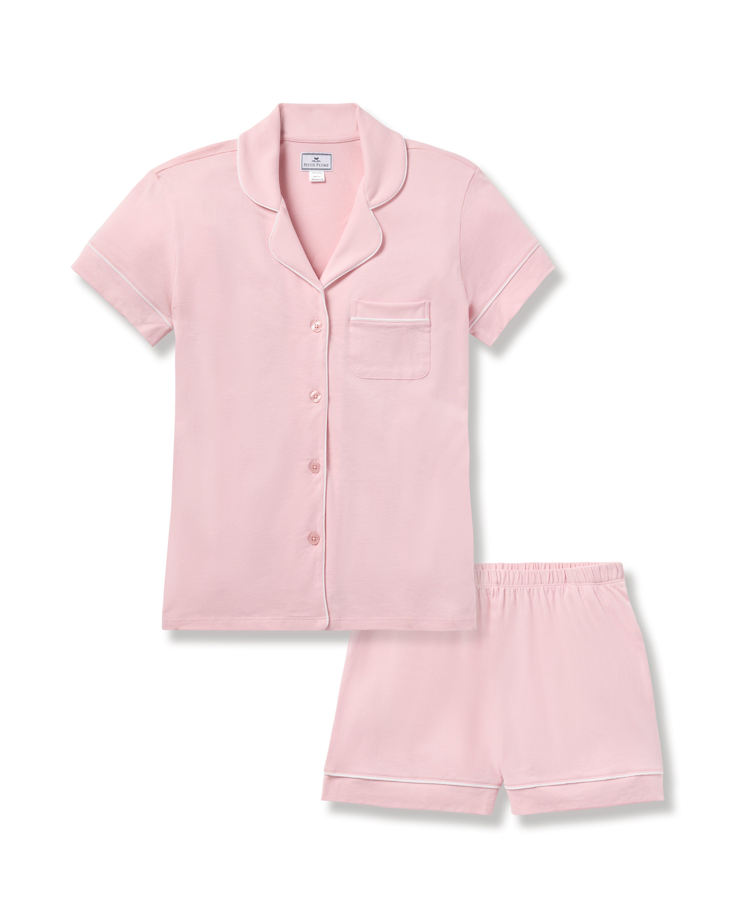 The Womens Pima Pajama Short Sleeve Set by Petite Plume, in light pink, is made of soft Peruvian Pima cotton. It includes a short-sleeve button-up top with a chest pocket and piped trim, paired with shorts featuring an elastic waistband and piped edges, all set against a white background.
