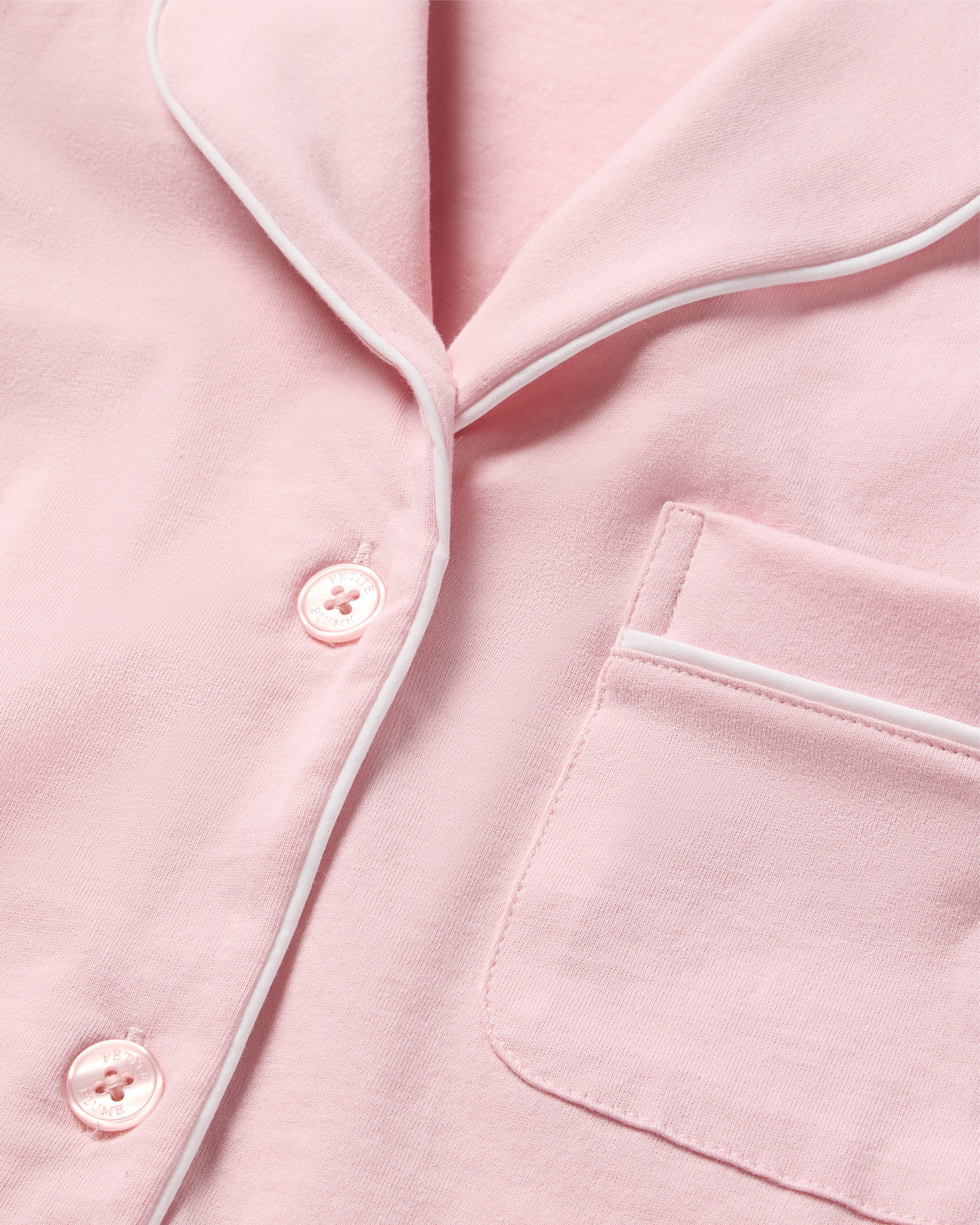 Close-up of the Womens Pima Pajama Short Sleeve Set in Pink by Petite Plume, showcasing a design with white piping, buttons, and a right-side pocket. Made from luxurious Peruvian Pima cotton, this soft fabric underscores elegant pajama top details.