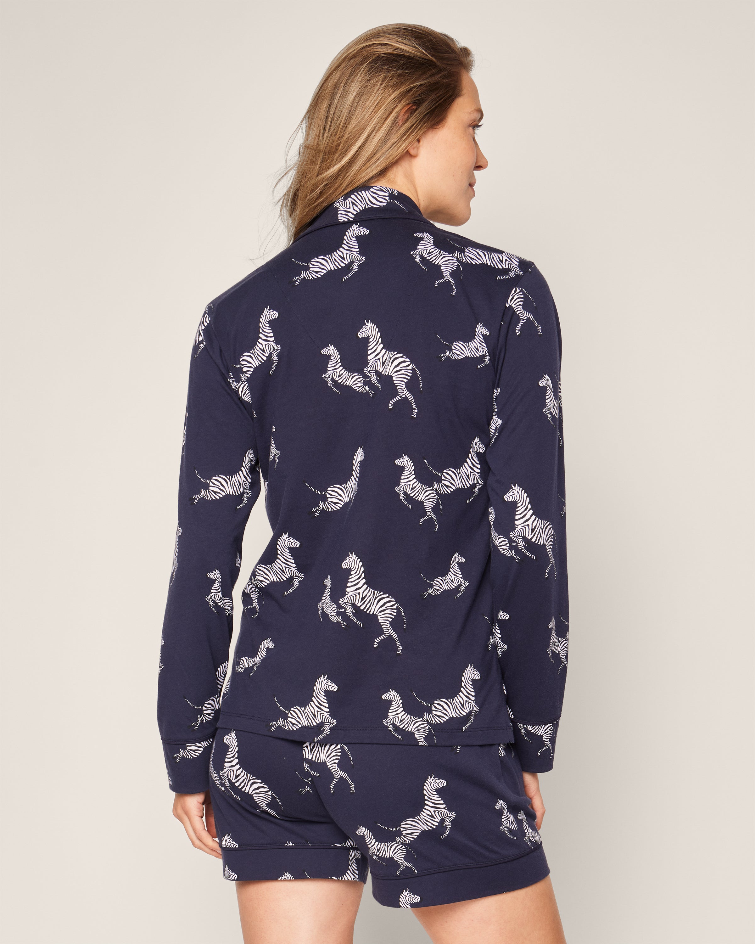 A person is seen from the back wearing a luxurious Womens Pima Long Sleeve Short Set in Zèbre de Nuit by Petite Plume, made from Peruvian Pima cotton with a white zebra print, set against a neutral light background.