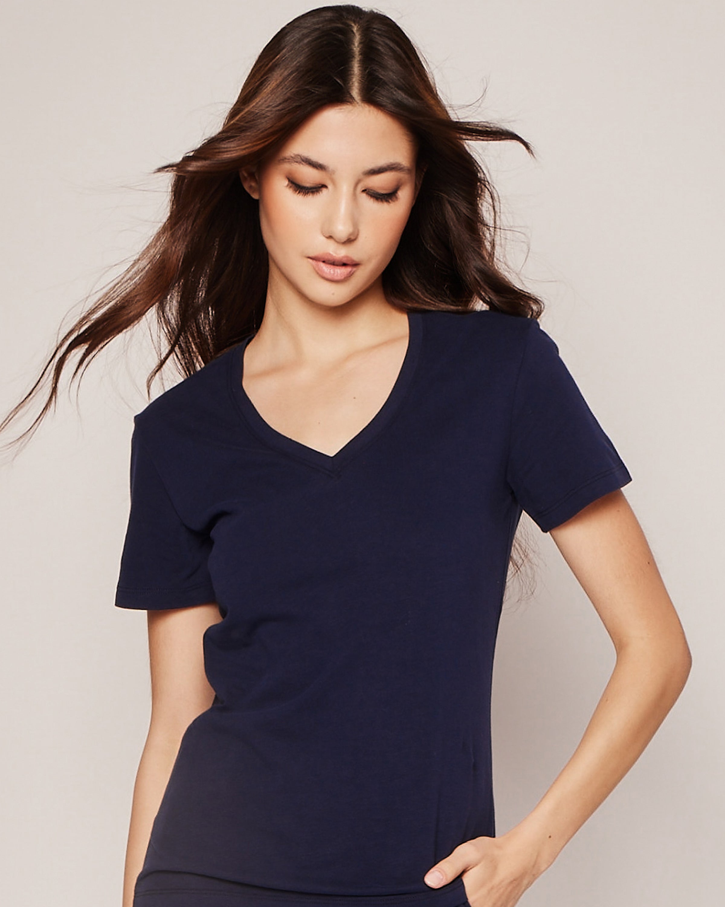 A person with long, dark hair wears the Petite Plume Womens Pima Short Sleeve Top in Navy, posing against a neutral background. The soft jersey knit fabric enhances their serene expression as their hair flows slightly, as if caught in a breeze.
