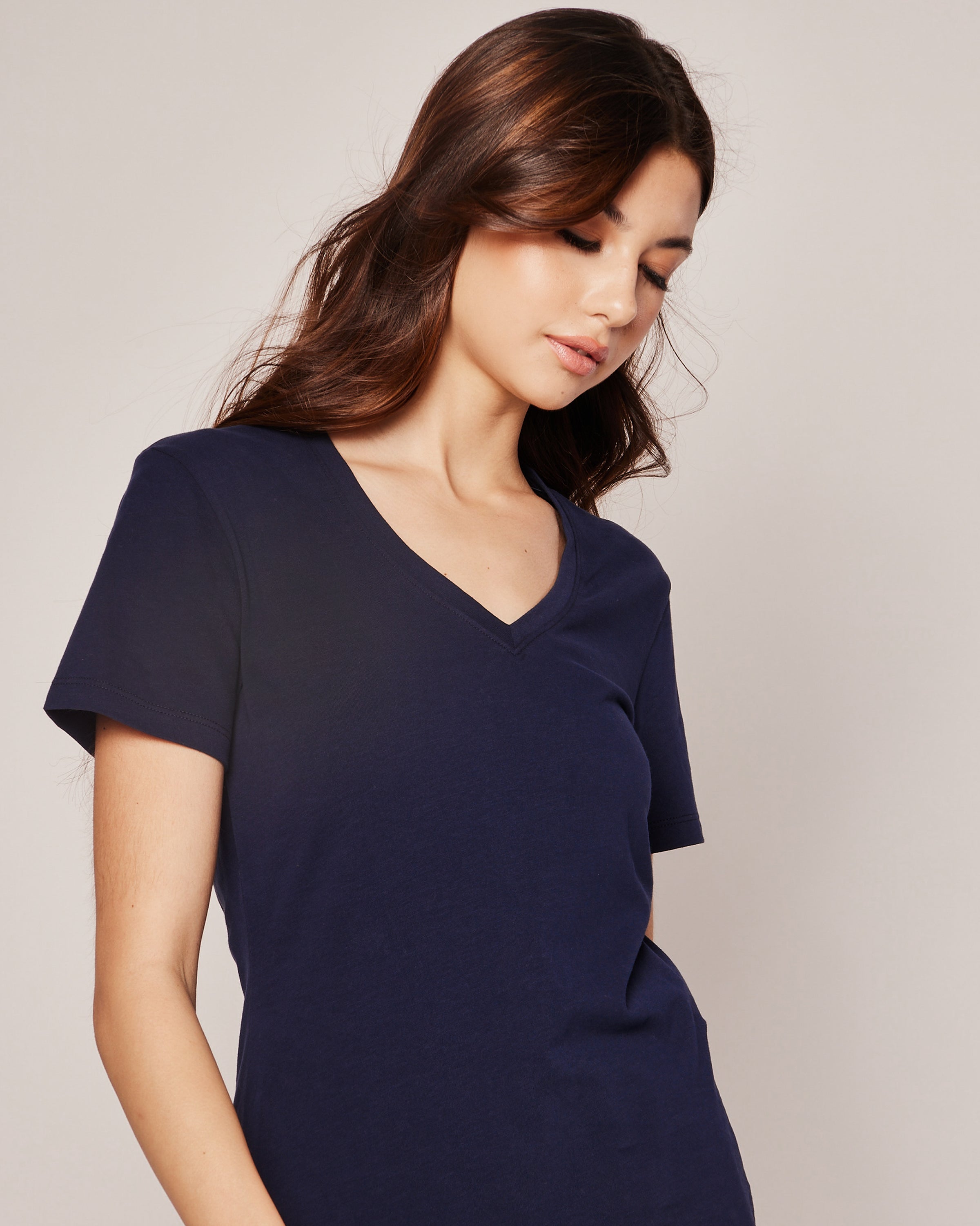 A woman with long brown hair wearing Petite Plumes Womens Pima Short Sleeve Top in Navy looks down slightly with a neutral expression against a plain, light-colored background.