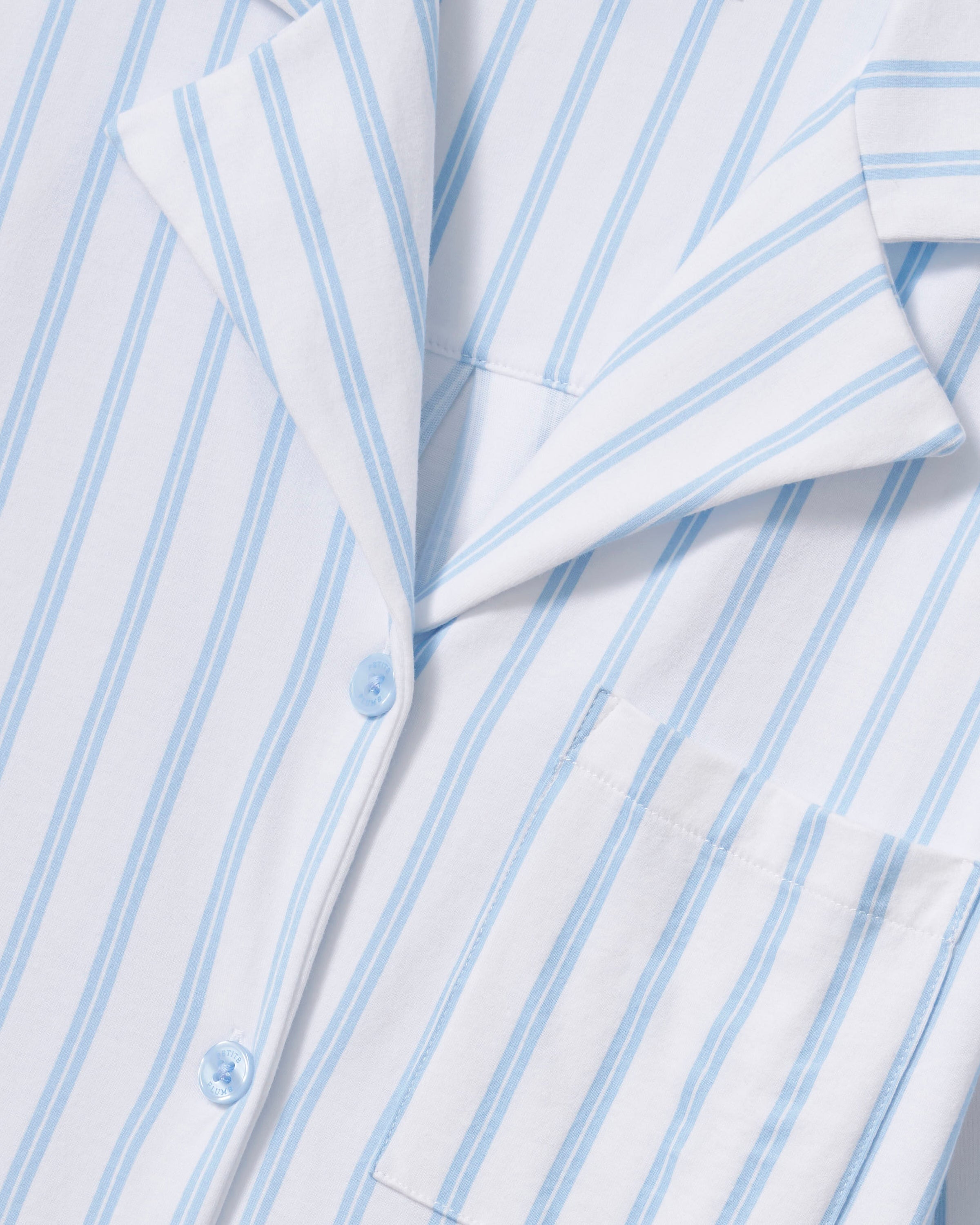 The Olivia Pima Short Set in Periwinkle Stripe features light blue and white vertical stripes, a short-sleeve button-up shirt with a chest pocket, and matching drawstring shorts.