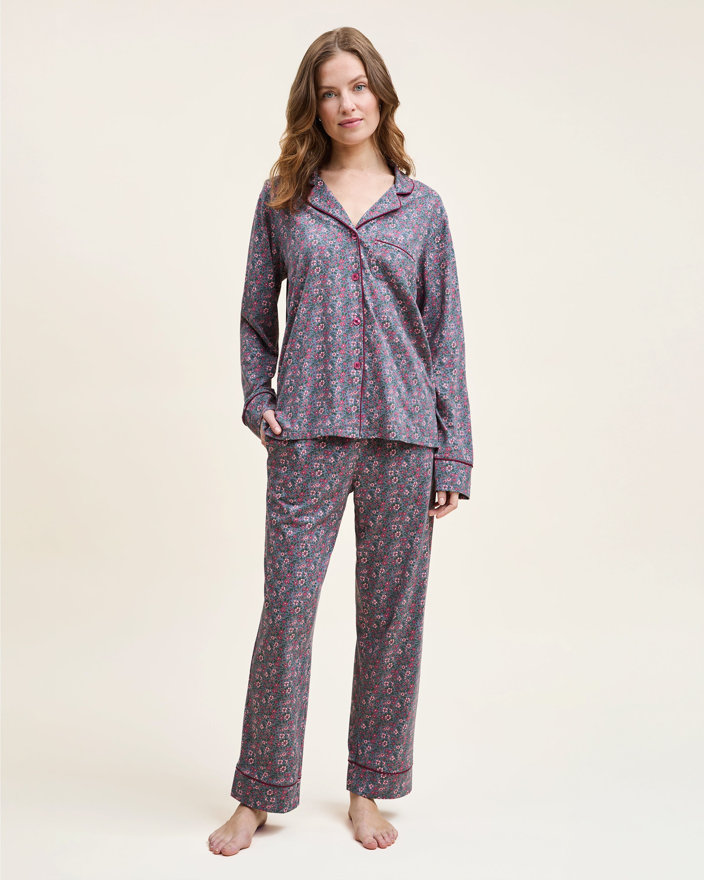 The Women's Pima Pajama Set in Fleurs de Saison features long sleeves and a small floral print in pink, white, and blue on gray. The set includes a button-up top with a chest pocket and matching pants.