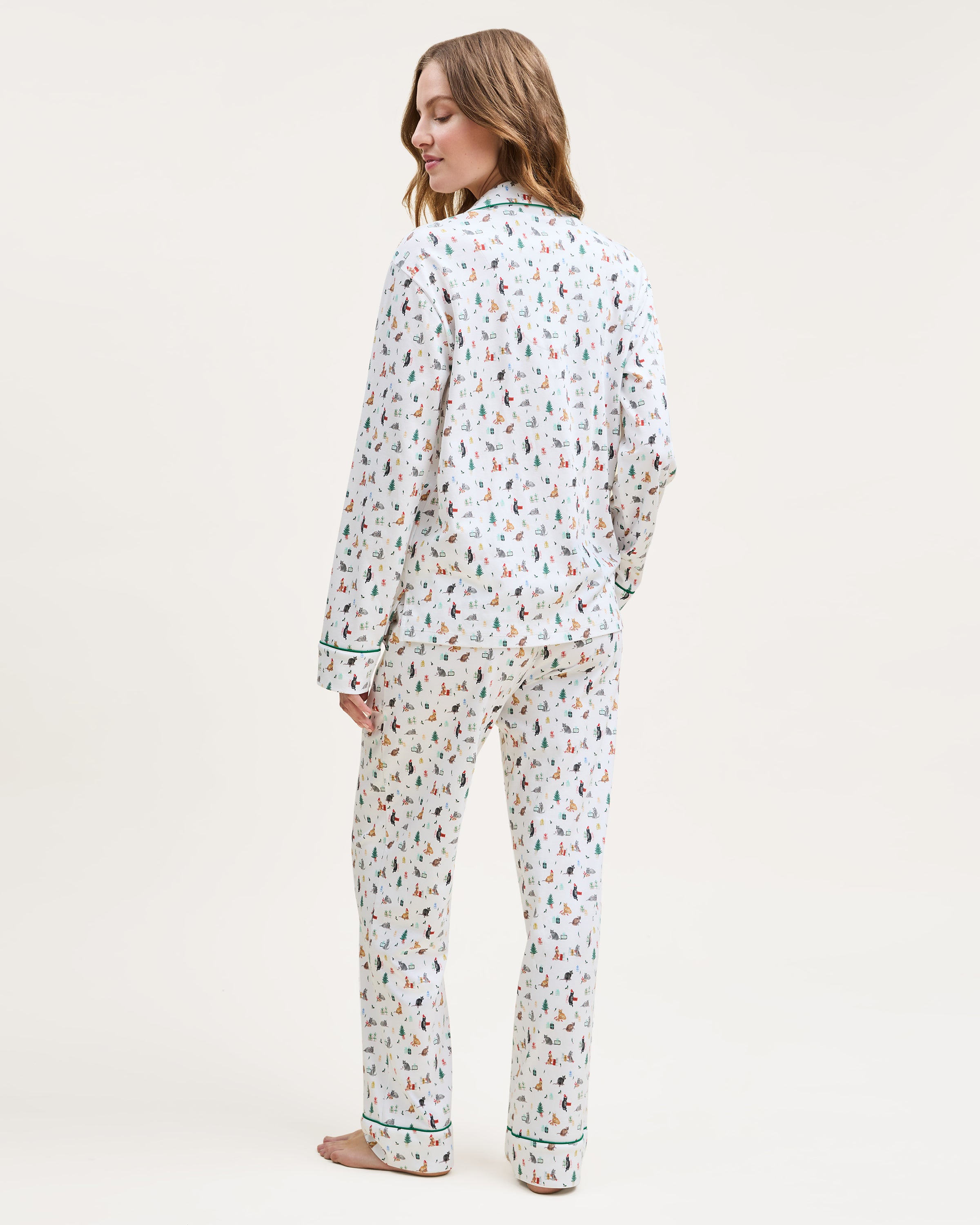 The Women's Pima Pajama Set in Merry Meow features a white, green-piped pajama set with a colorful cat print. Includes a long-sleeve button-up top with chest pocket and matching pants.