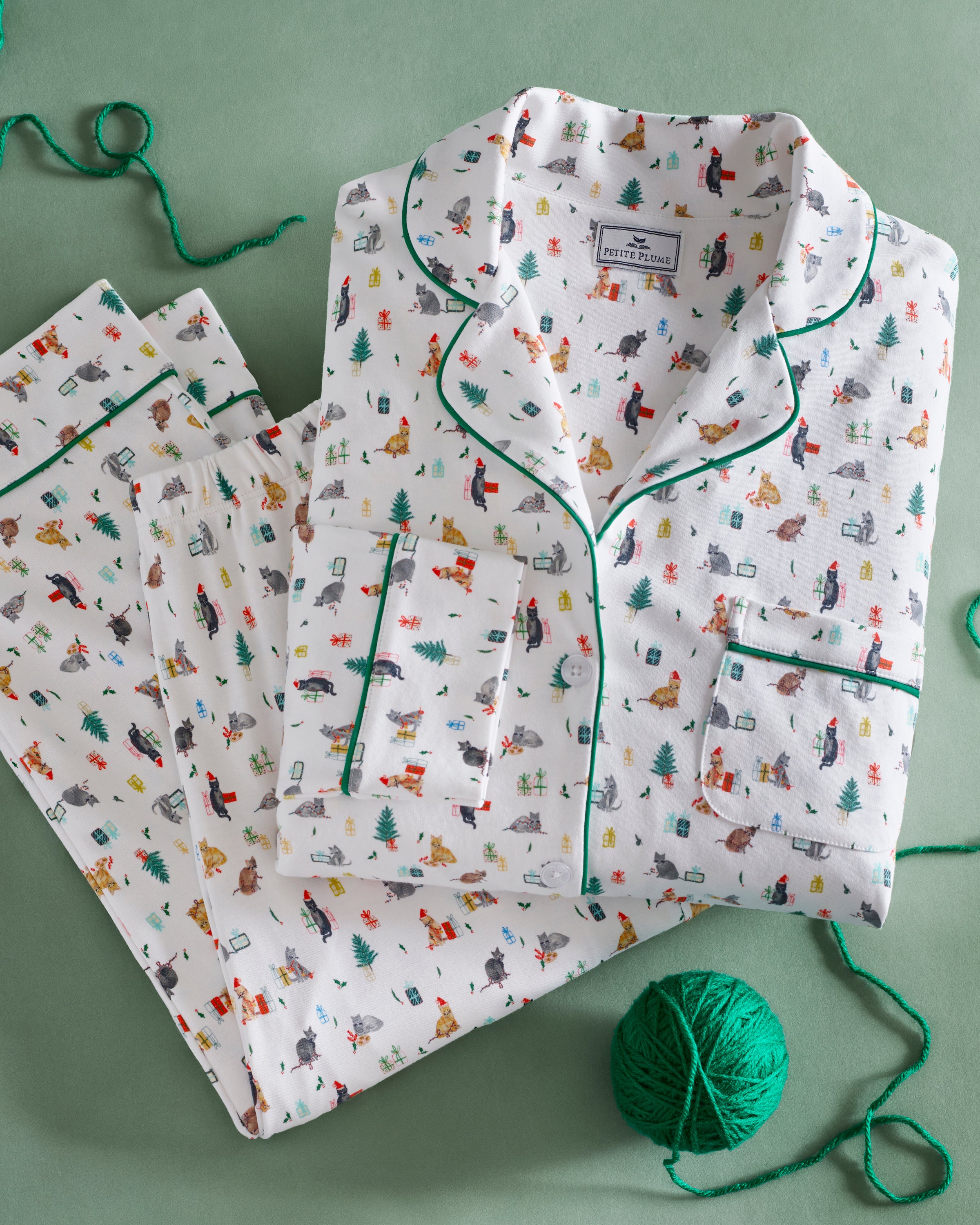 The Women's Pima Pajama Set in Merry Meow features a white, green-piped pajama set with a colorful cat print. Includes a long-sleeve button-up top with chest pocket and matching pants.