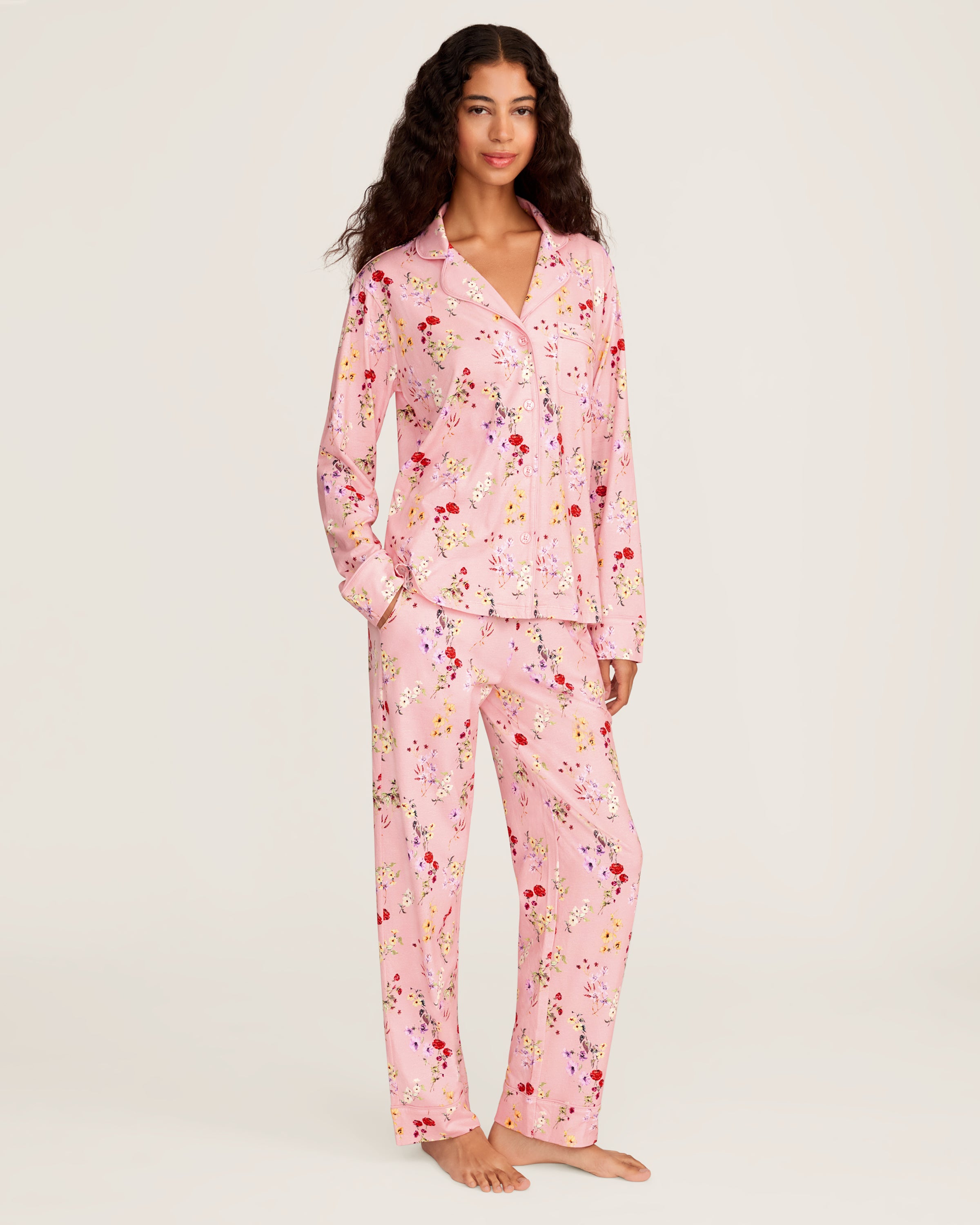 The Women's Pima Pajama Set in Brilliant Botanical Blush features a pink button-up long-sleeve top and matching pants, both adorned with a vibrant floral print in red, white, and purple.