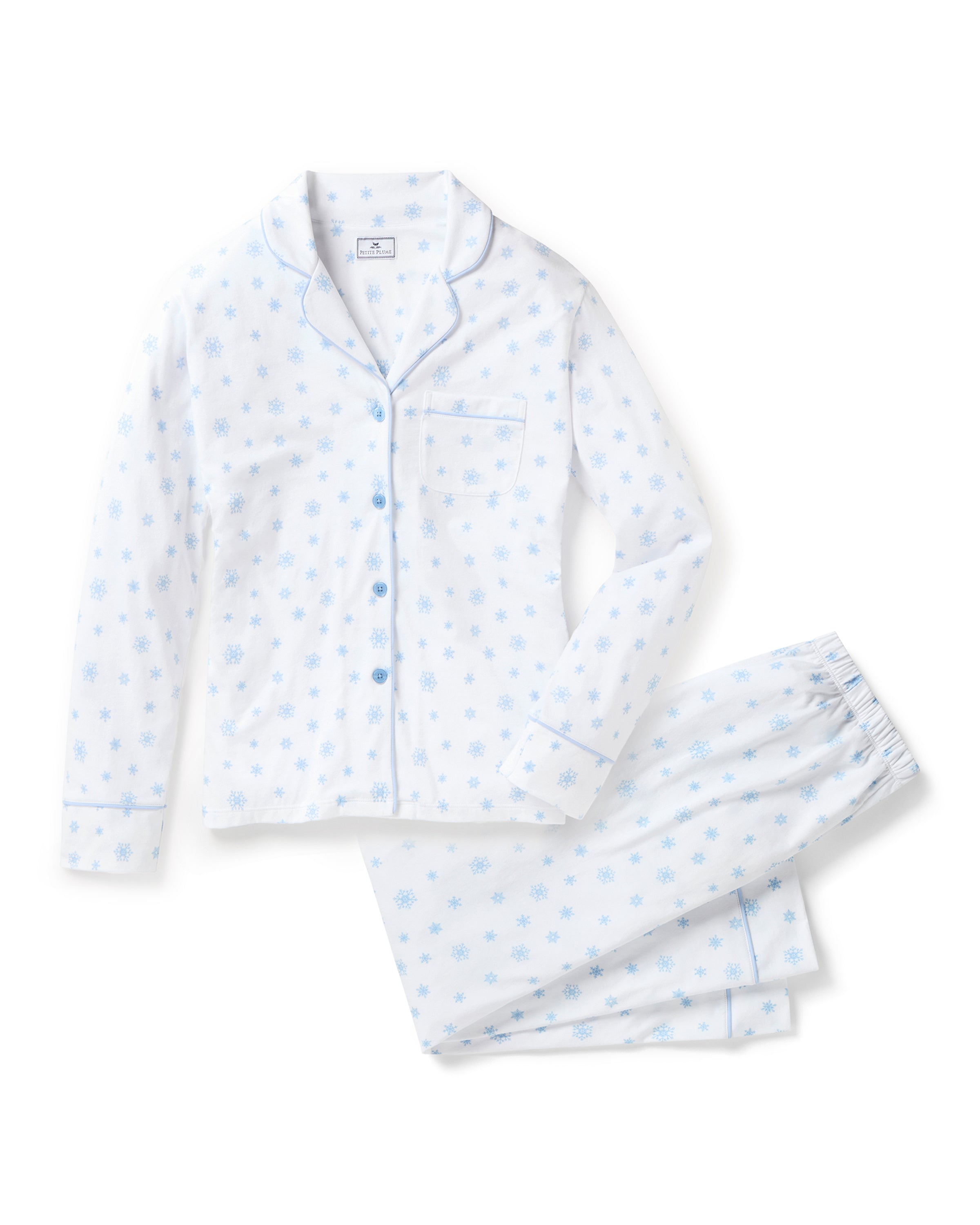 The Women's Pima Pajama Set in Periwinkle Wonderland features white pajamas with light blue snowflake patterns, a collared long-sleeve button-up top with pocket, and matching elastic waist pants, both accented with blue piping.