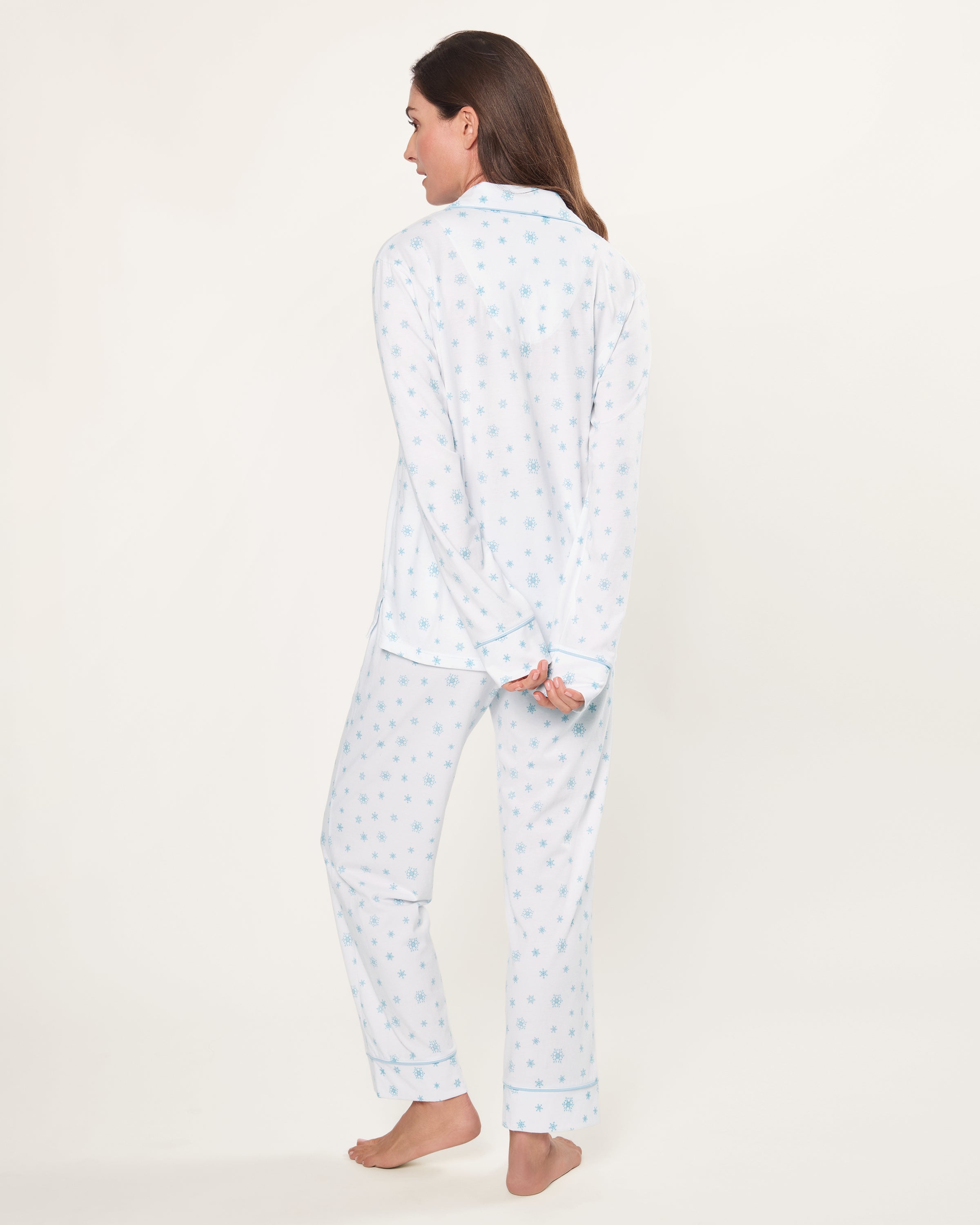 The Women's Pima Pajama Set in Periwinkle Wonderland features white pajamas with light blue snowflake patterns, a collared long-sleeve button-up top with pocket, and matching elastic waist pants, both accented with blue piping.