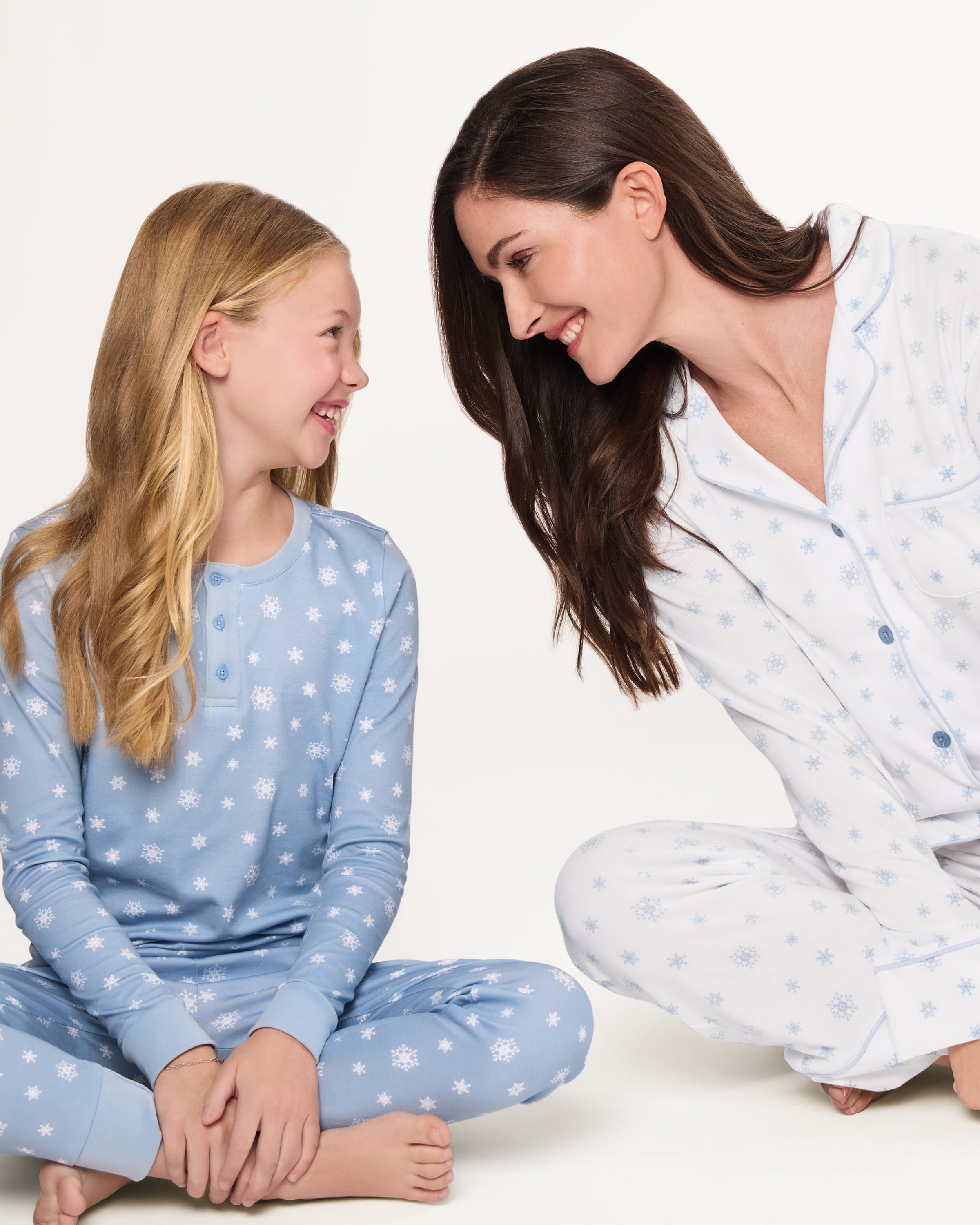 The Women's Pima Pajama Set in Periwinkle Wonderland features white pajamas with light blue snowflake patterns, a collared long-sleeve button-up top with pocket, and matching elastic waist pants, both accented with blue piping.