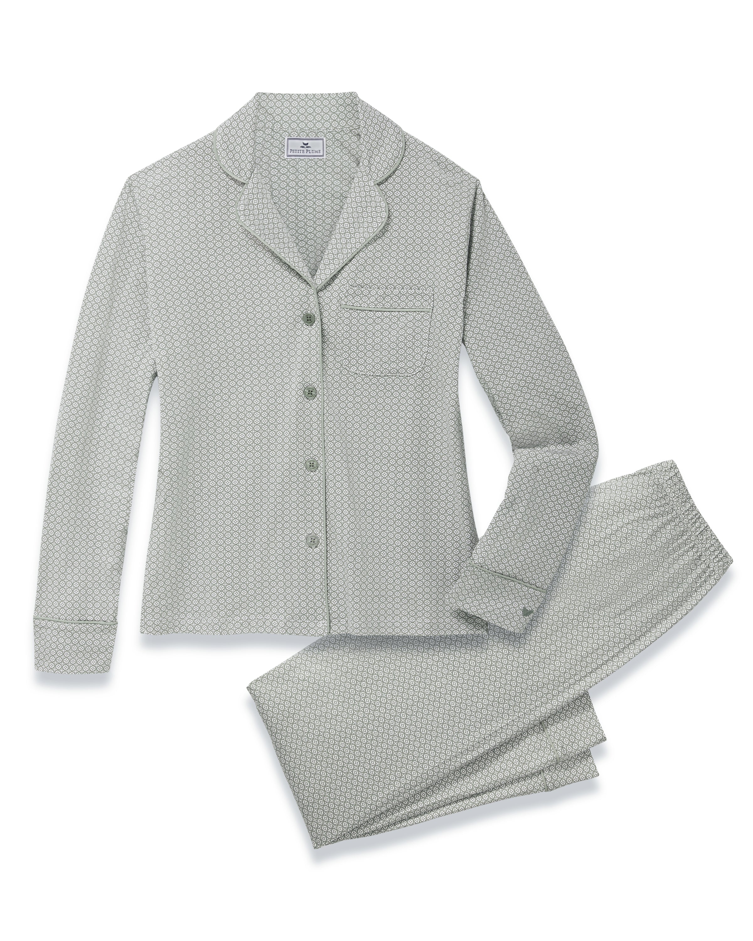 A woman with long curly hair stands barefoot against a white background, wearing the Women's Lightweight Pima Pajama Set in Sage Geo—a light gray button-up long-sleeve top and matching pants with a small geometric pattern.