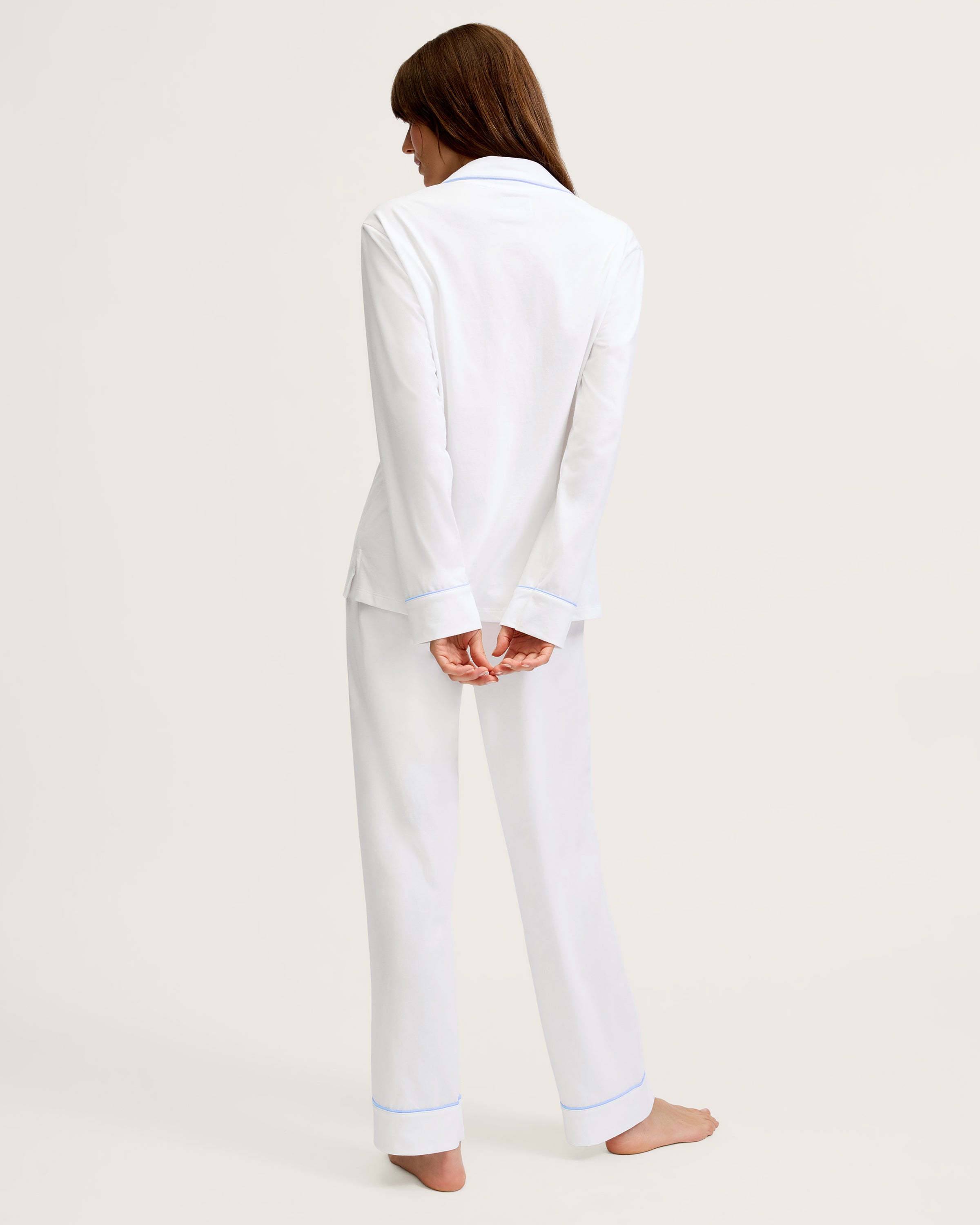 The Women's Pima Pajama Set in White with Periwinkle Piping features a long-sleeve button-up top with a chest pocket and matching pants, both trimmed with periwinkle piping along the collar, cuffs, pocket, and pant hems.