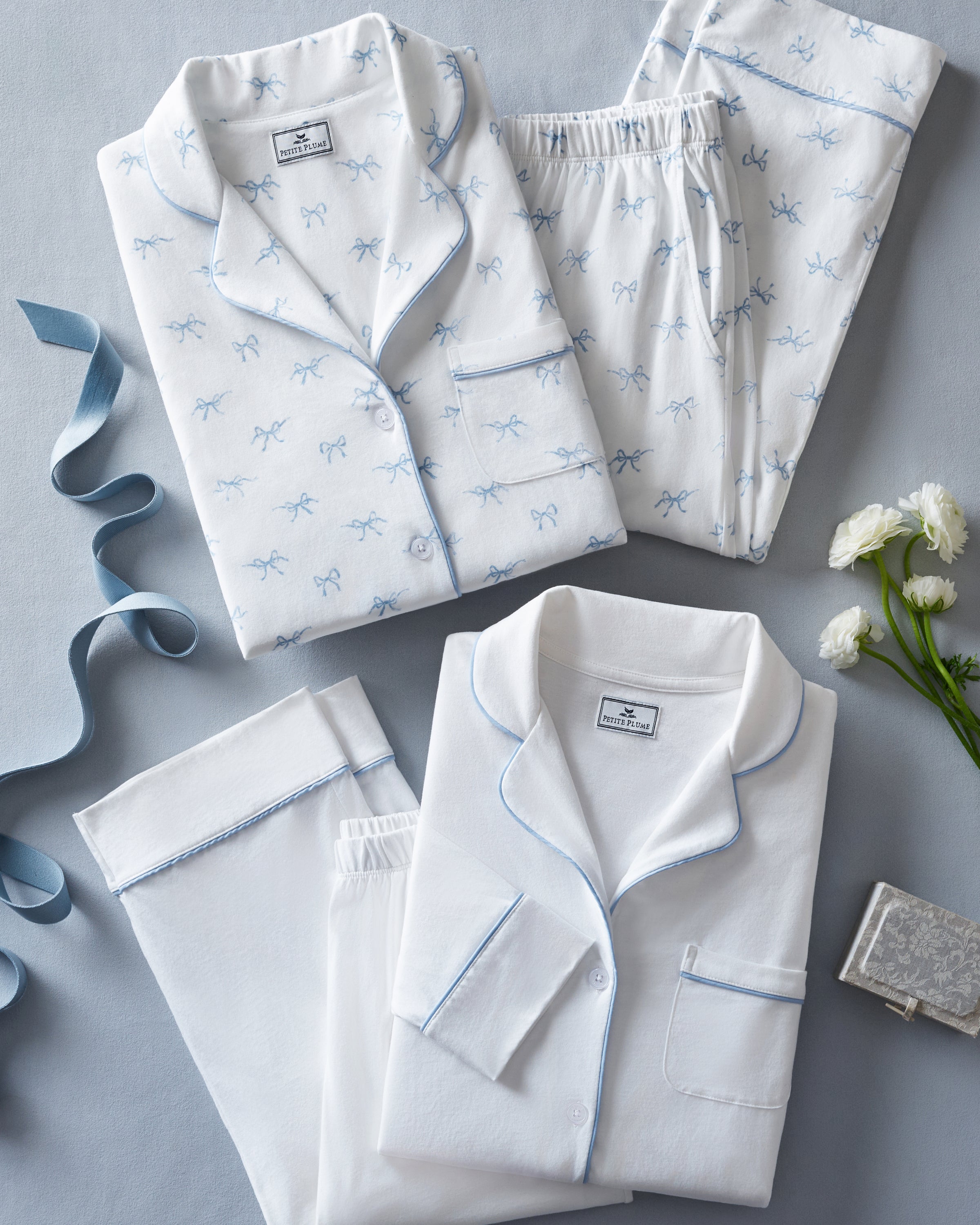 The Women's Pima Pajama Set in White with Periwinkle Piping features a long-sleeve button-up top with a chest pocket and matching pants, both trimmed with periwinkle piping along the collar, cuffs, pocket, and pant hems.