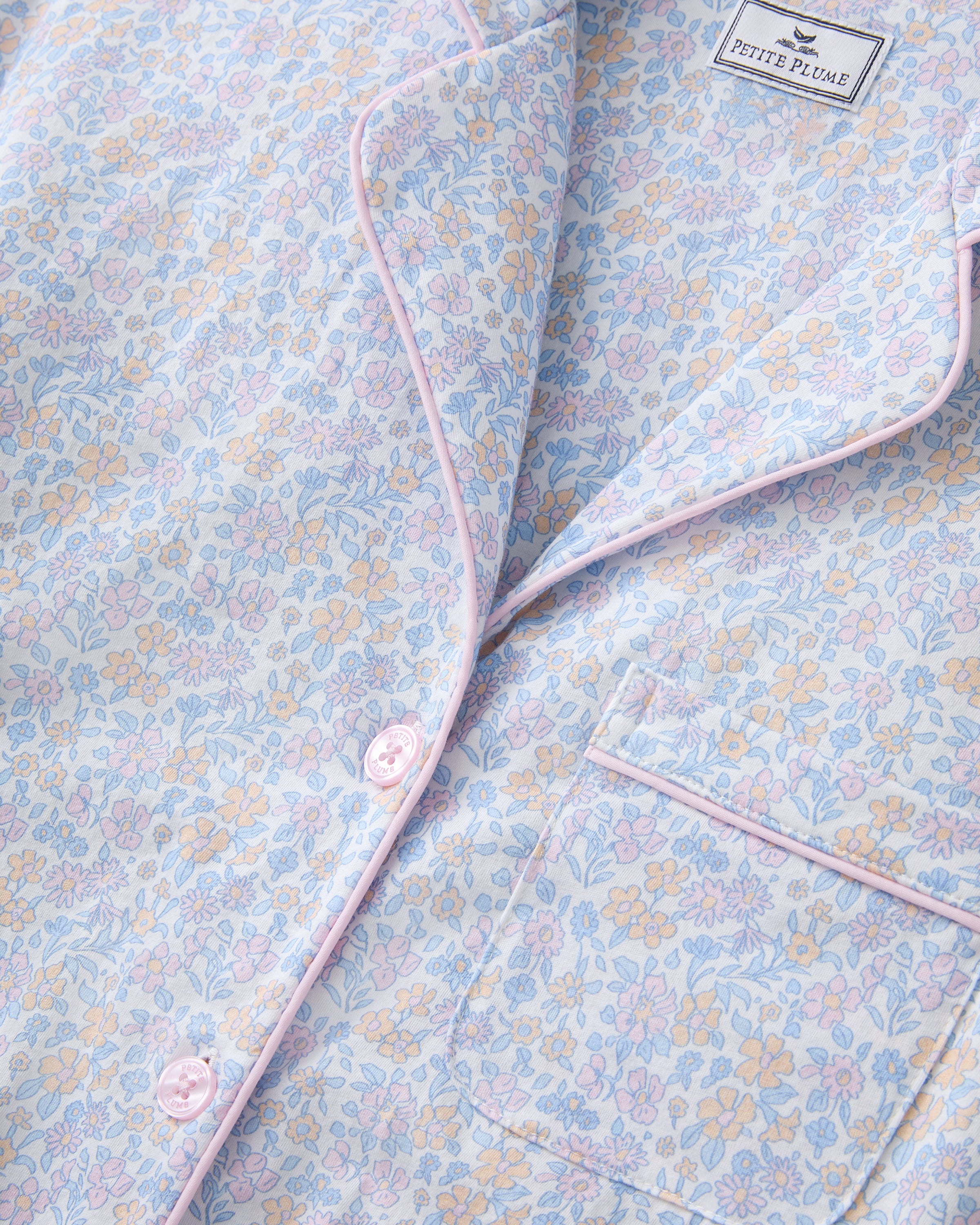 A woman with long wavy hair wears the Women's Lightweight Pima Short Sleeve Short Set in Fleur Blanche, featuring a pastel floral pattern, standing against a plain background.