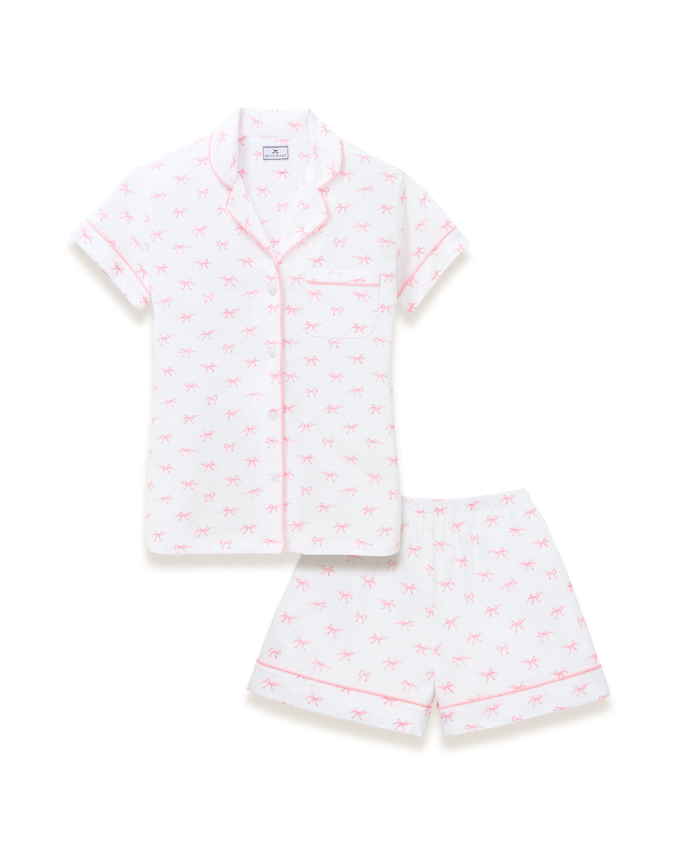 The Women's Pima Short Sleeve Short Set in Blushing Bows features a white button-up top with pink piping, a front pocket, and matching shorts, all adorned with an all-over pink bow pattern.