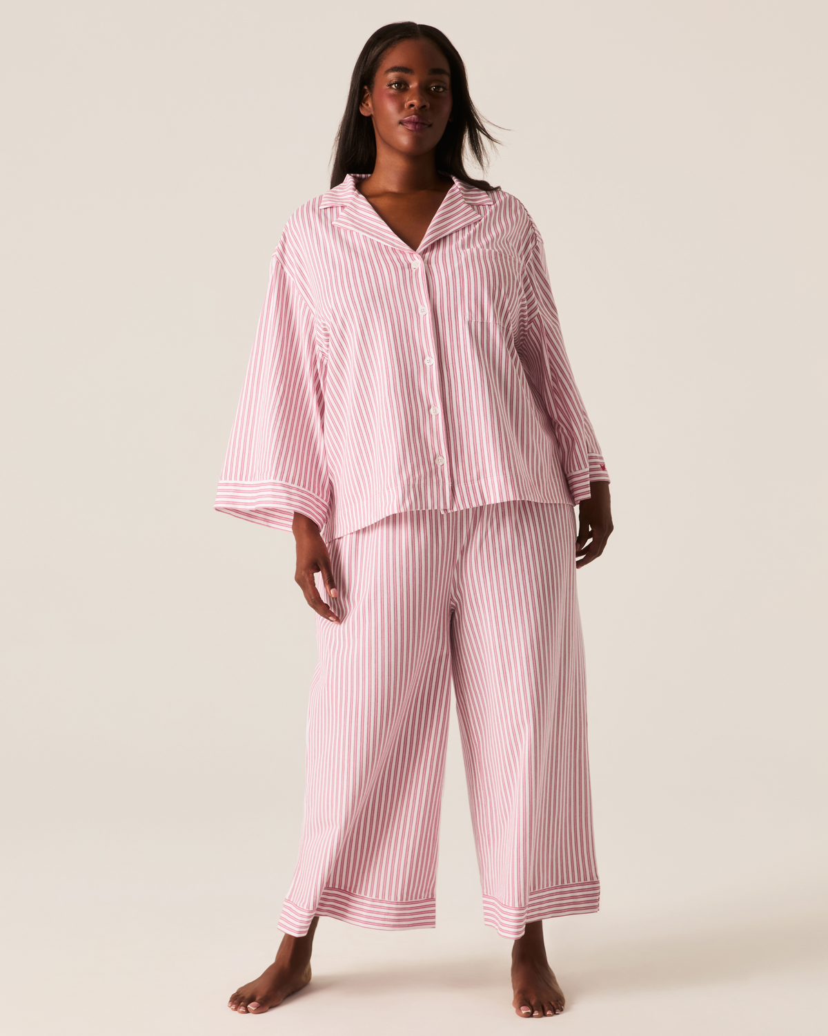 A person wearing The Olivia Wide Leg Pima Pajama Set in Antique Red Ticking, featuring a long-sleeved button-up top and matching wide-leg trousers in a red and white striped pattern.