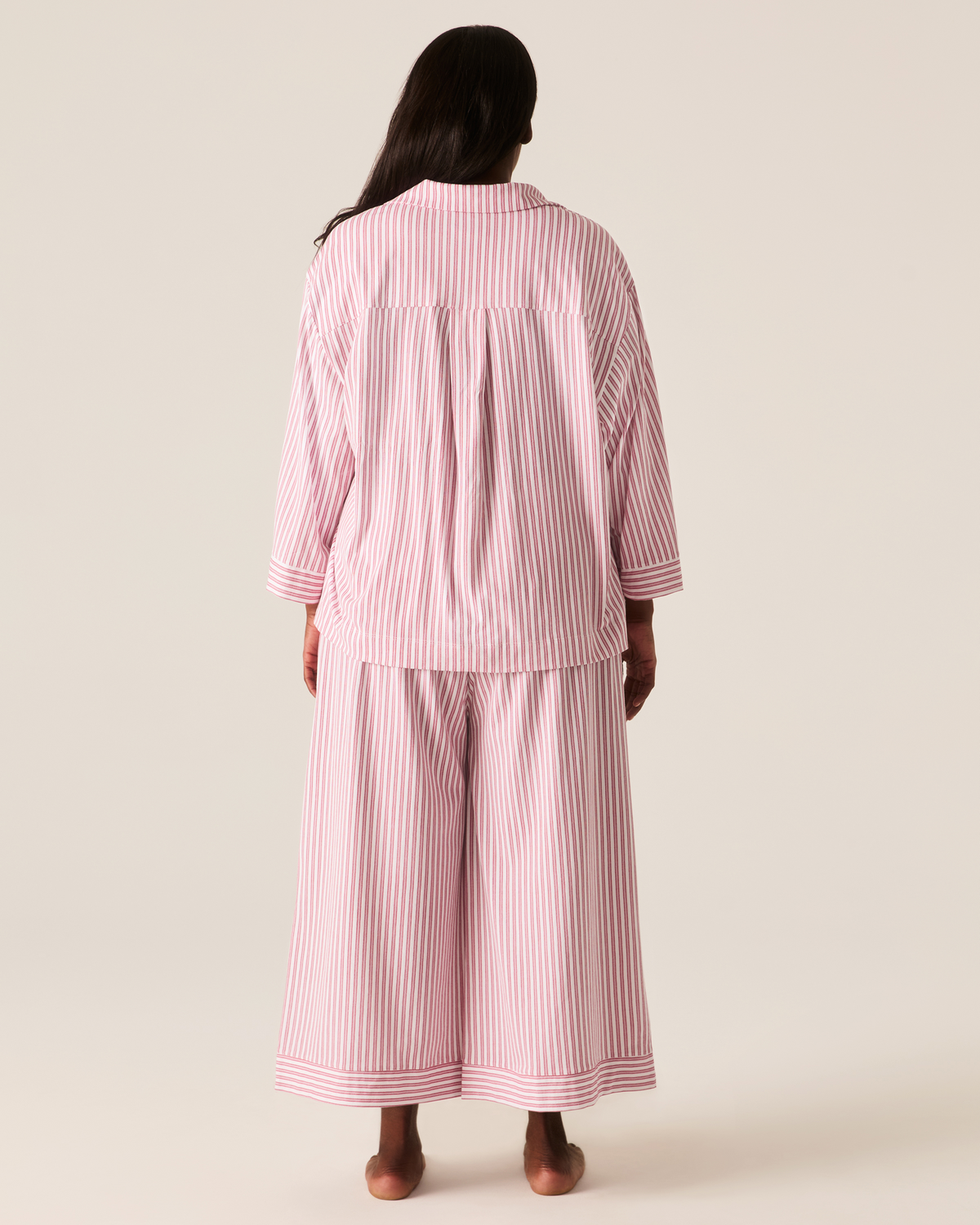 Back view of a person wearing The Olivia Wide Leg Pima Pajama Set in Antique Red Ticking, featuring a red and white vertical-striped button-down shirt and wide-leg trousers.