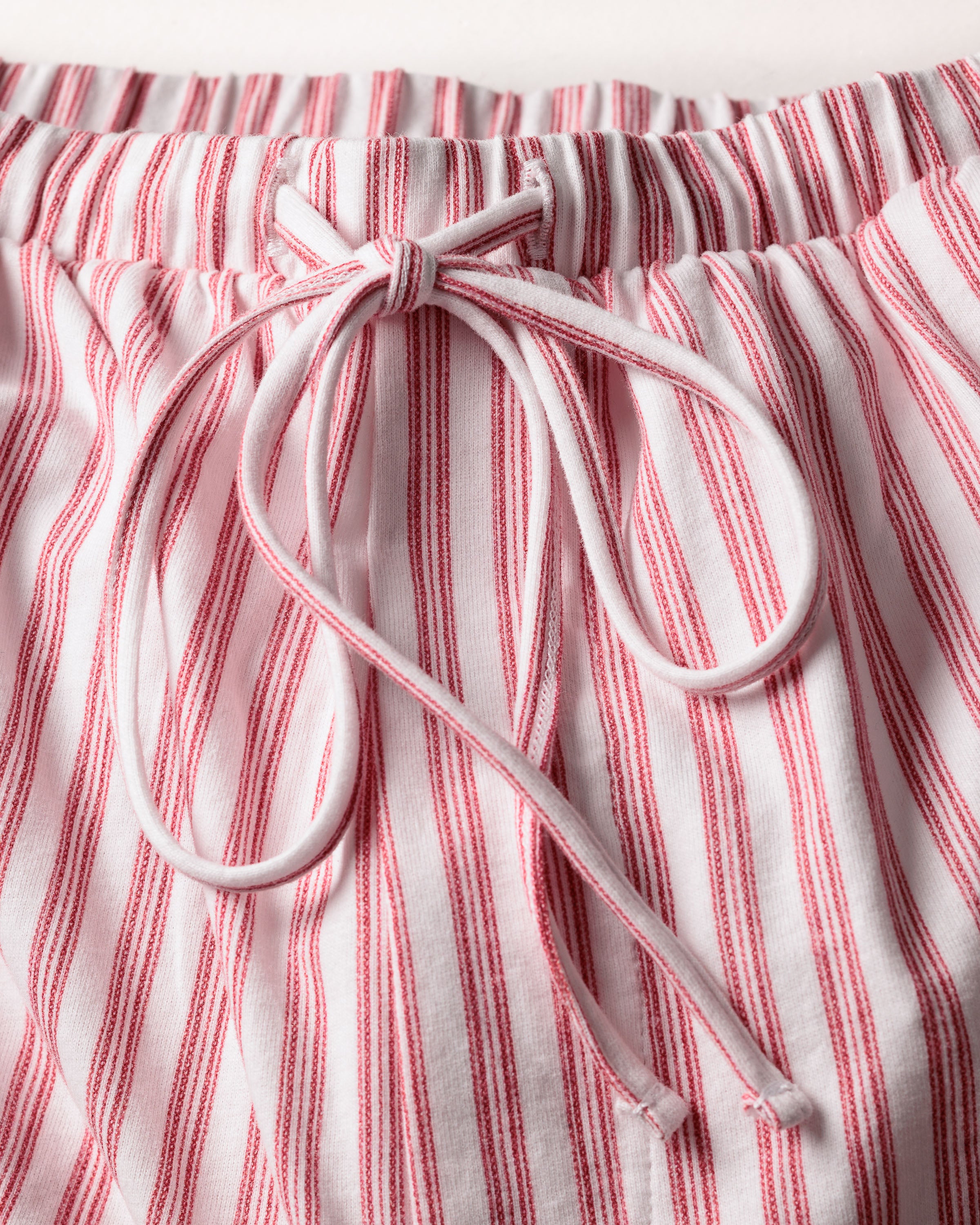 Close-up of The Olivia Wide Leg Pima Pajama Set in Antique Red Ticking by Petite Plume, showcasing white Peruvian Pima cotton pants with vertical red stripes and a drawstring waist tied in a bow, complemented by an elastic waistband.