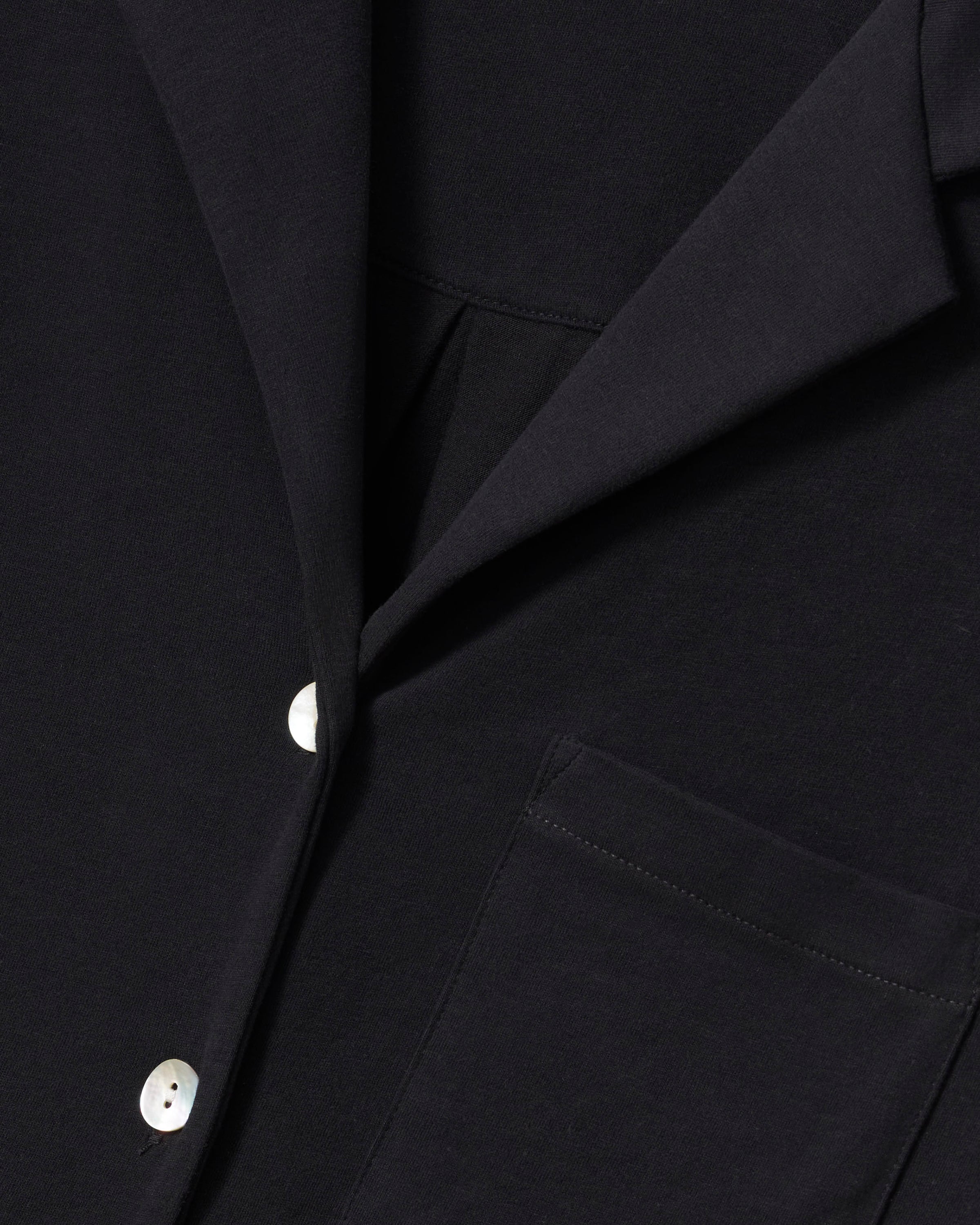 Modeling relaxed elegance, a person poses barefoot against an off-white background in The Olivia Wide Leg Pima Pajama Set from Petite Plume, featuring a loose-fitting black button-up top and wide-legged pants crafted from luxurious Peruvian Pima cotton.