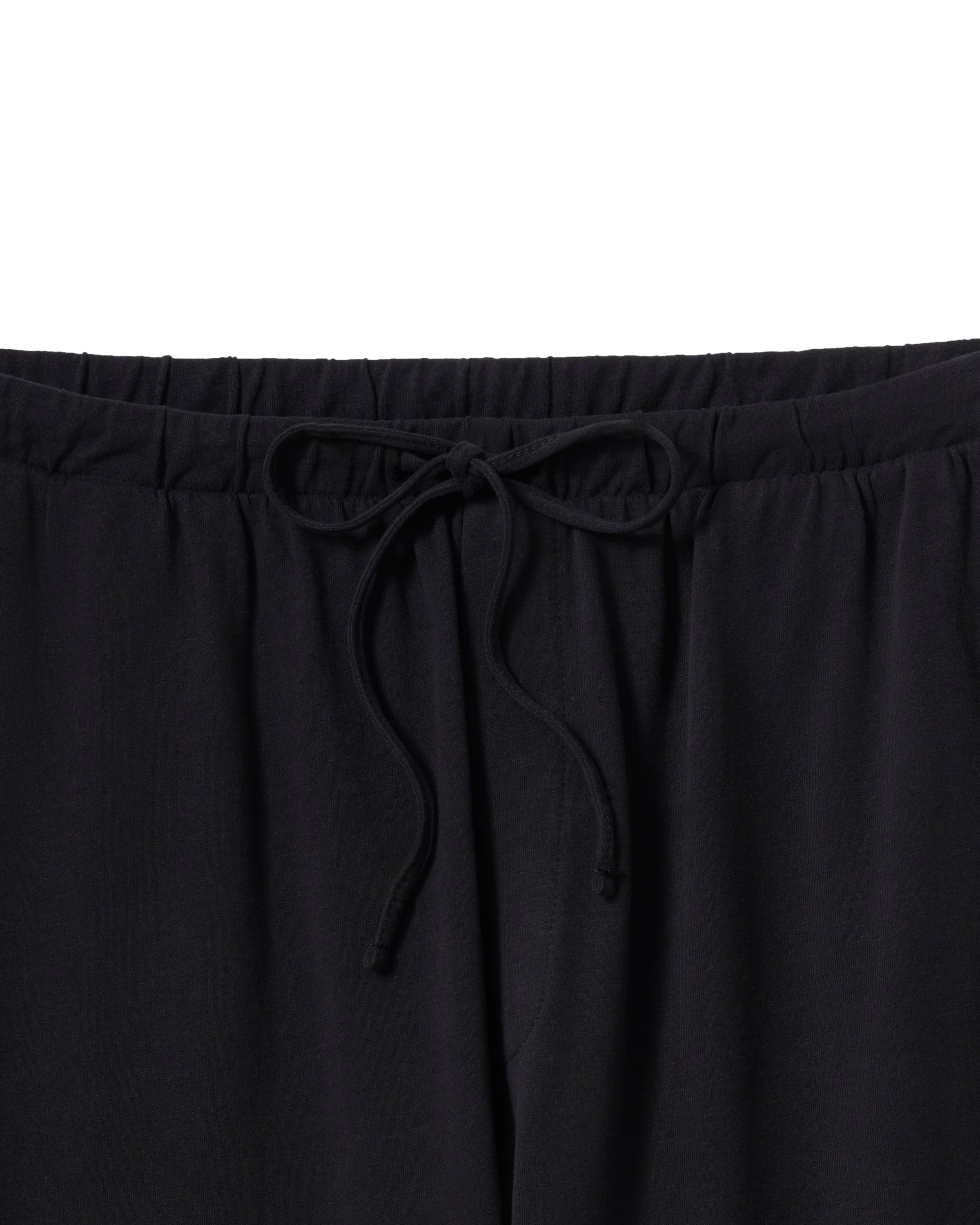 Modeling relaxed elegance, a person poses barefoot against an off-white background in The Olivia Wide Leg Pima Pajama Set from Petite Plume, featuring a loose-fitting black button-up top and wide-legged pants crafted from luxurious Peruvian Pima cotton.