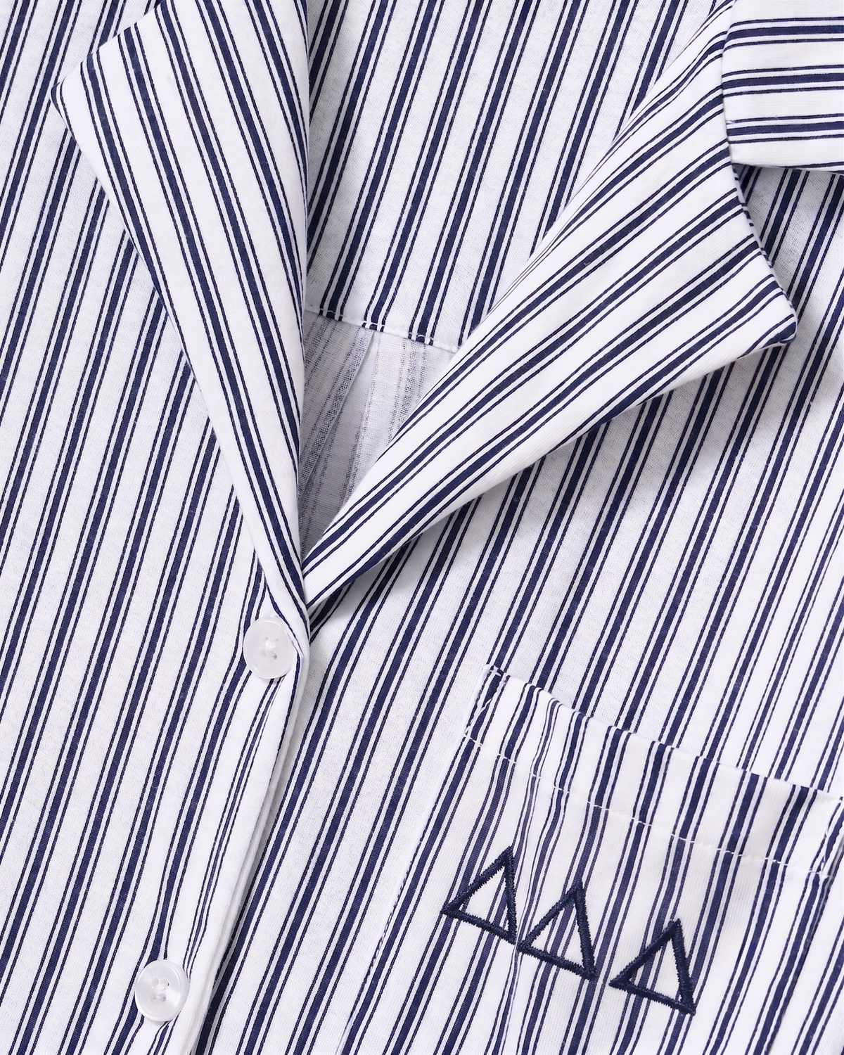 Close-up of the Greek Embroidered Olivia Wide Leg Pima Pajama Set in Navy French Ticking, featuring a white shirt with thin black vertical stripes, white buttons, a pocket, and three black embroidered triangle shapes on the pocket.