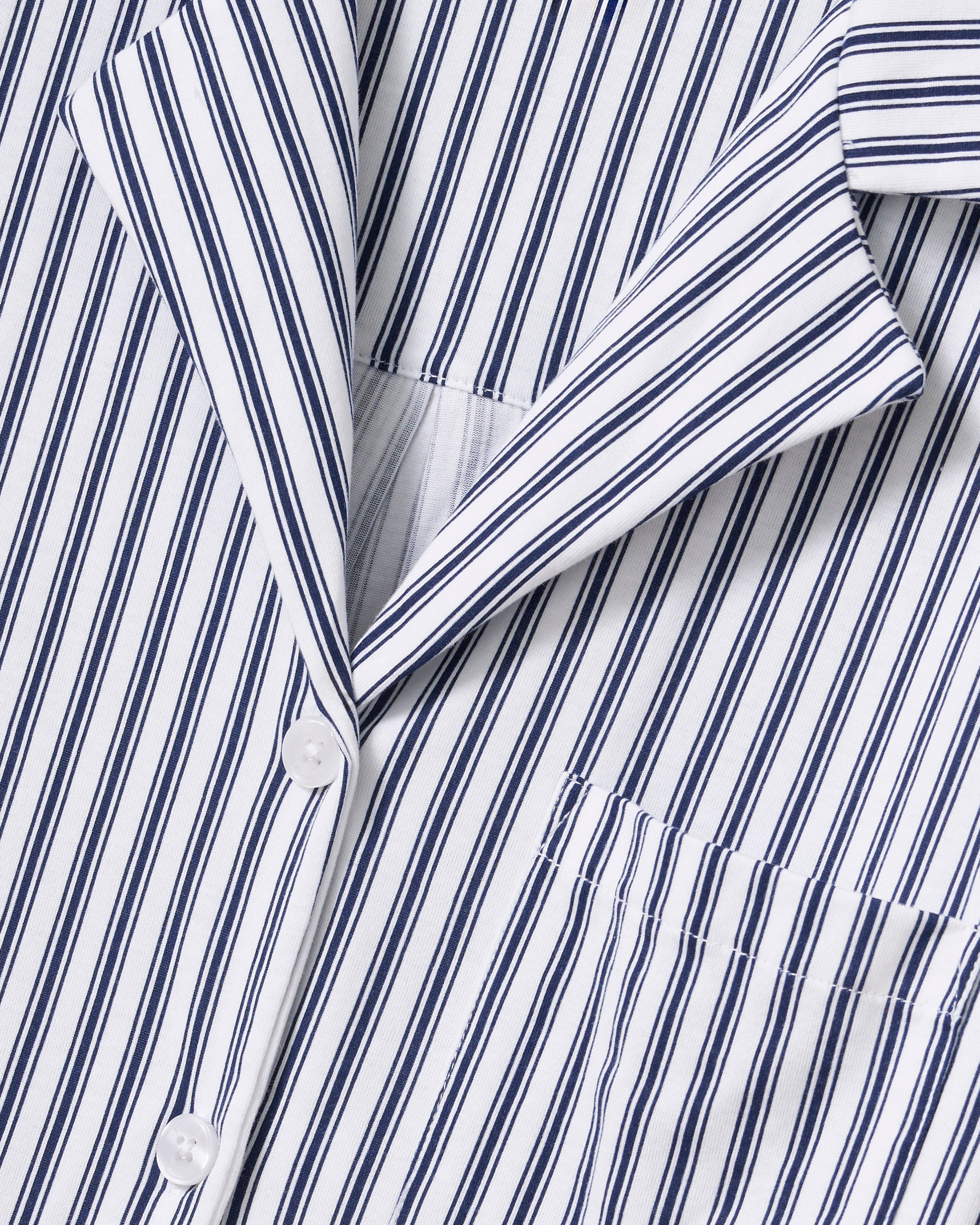 A person with long dark hair is wearing Petite Plumes Olivia Wide Leg Pima Pajama Set in Navy French Ticking, crafted from luxurious Peruvian Pima cotton. The button-up shirt and wide-legged pants have vertical stripes in alternating dark and light colors. They stand barefoot against a plain background.