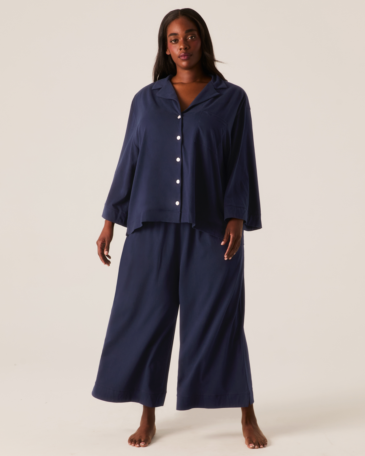 A person wearing The Olivia Wide Leg Pima Pajama Set in navy, featuring a button-down collared shirt and wide-leg trousers.