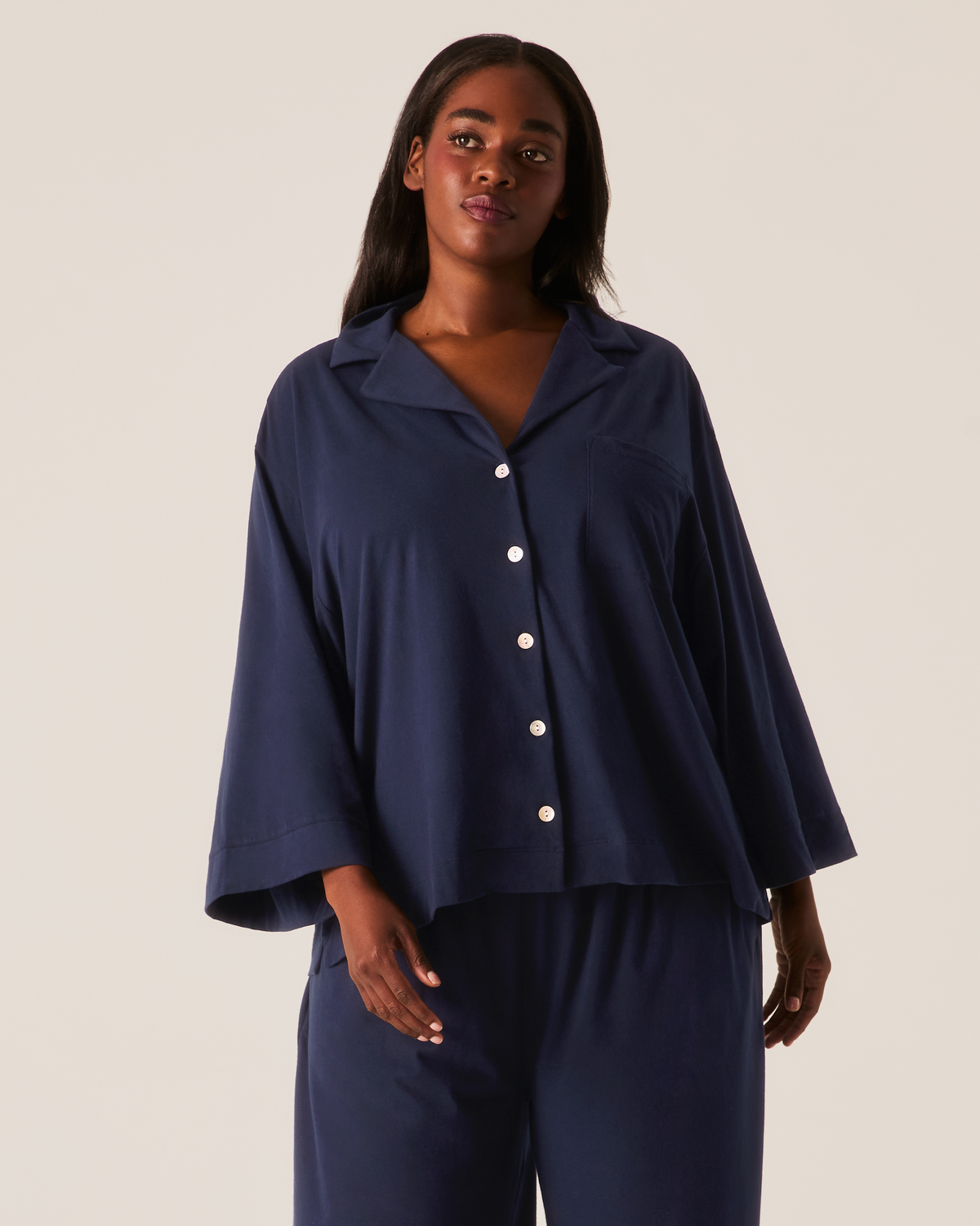 A person wearing The Olivia Wide Leg Pima Pajama Set in Navy, featuring a button-up shirt with a collar and wide sleeves paired with matching wide-leg pants.