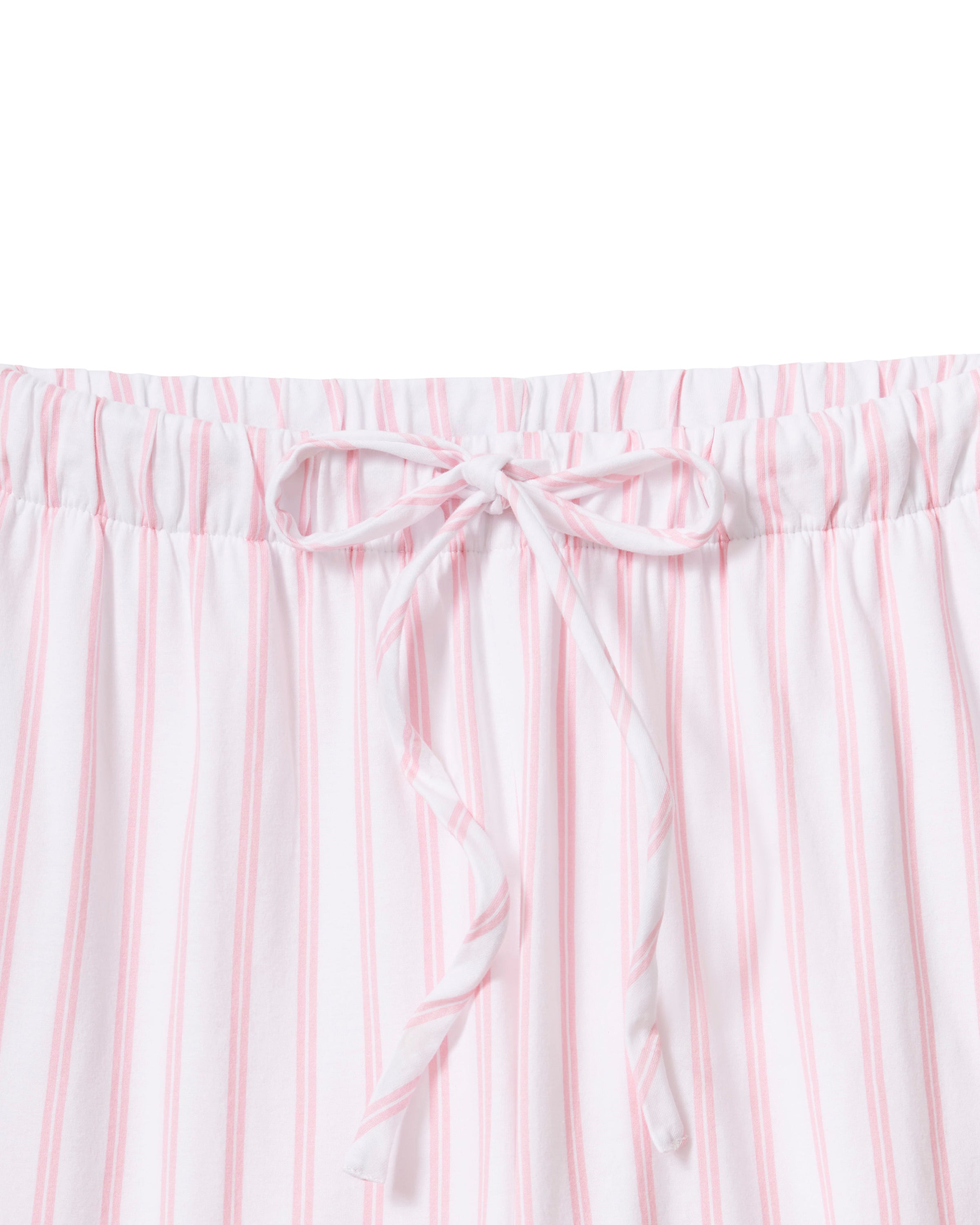 A person is seen in The Olivia Wide Leg Pima Pajama Set in Pink Stripe by Petite Plume, featuring a button-up top with a collar and long sleeves, and wide-leg pants made of luxurious Peruvian Pima cotton. The backdrop is plain and light-colored.